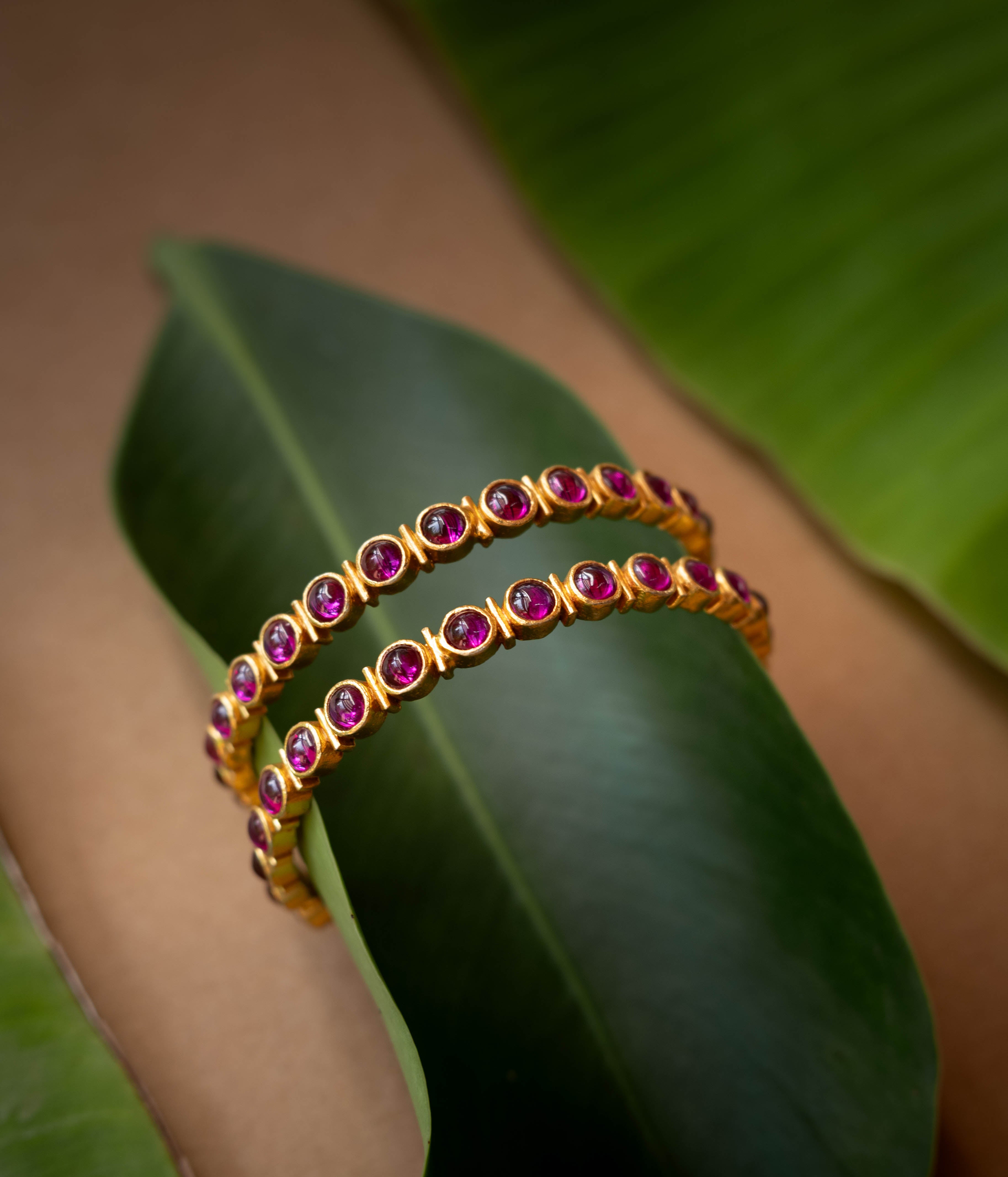A gold-toned hinged bangle with a row of red stones in the center.
