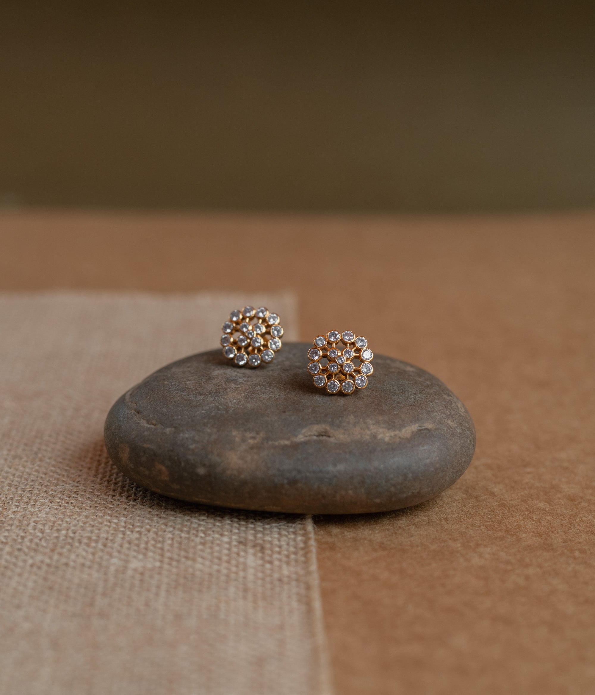 Gold floral stud earrings set with clear Swarovski stones, on a rock surface.