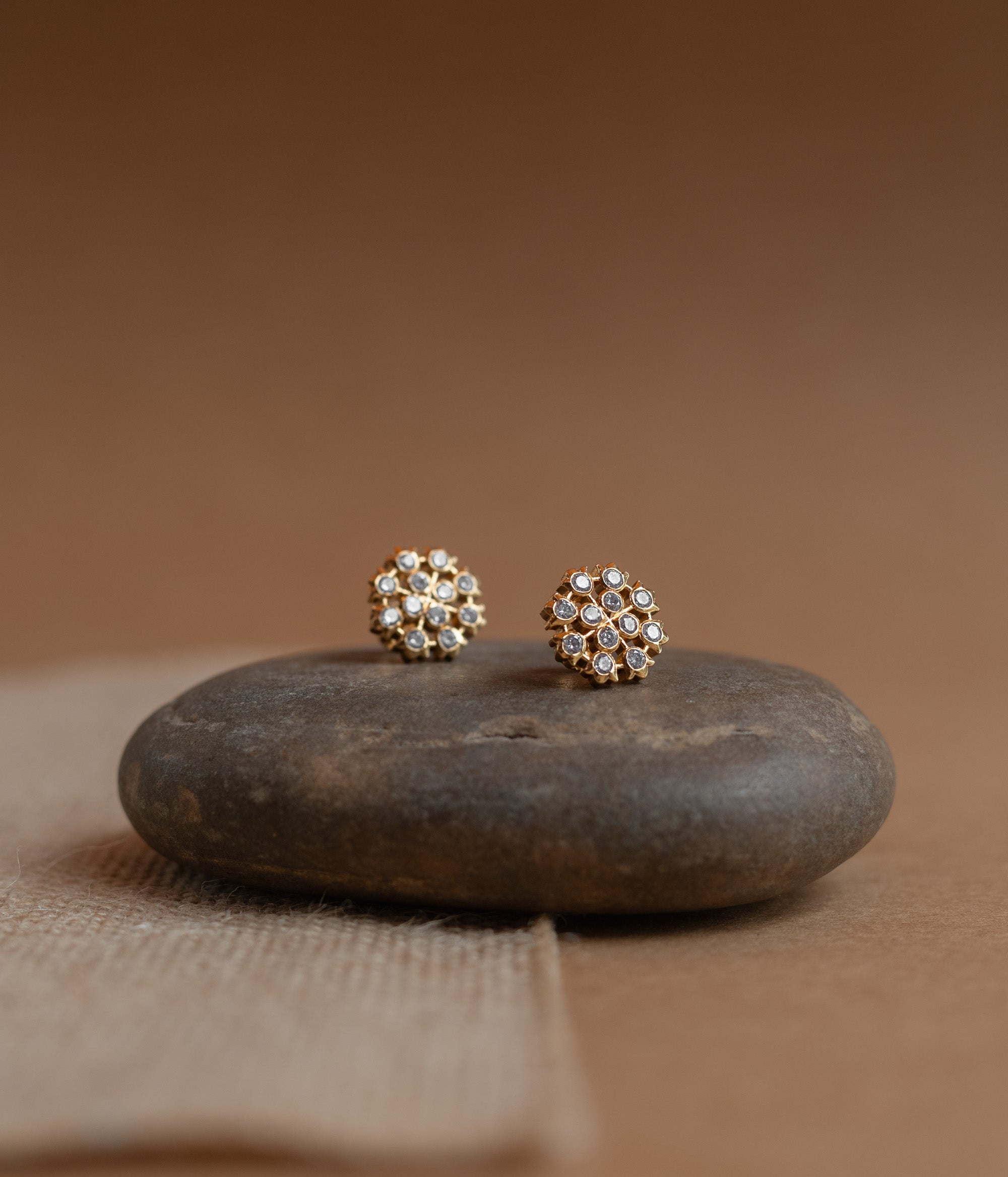 Gold floral stud earrings set with clear Swarovski stones, on a rock surface.