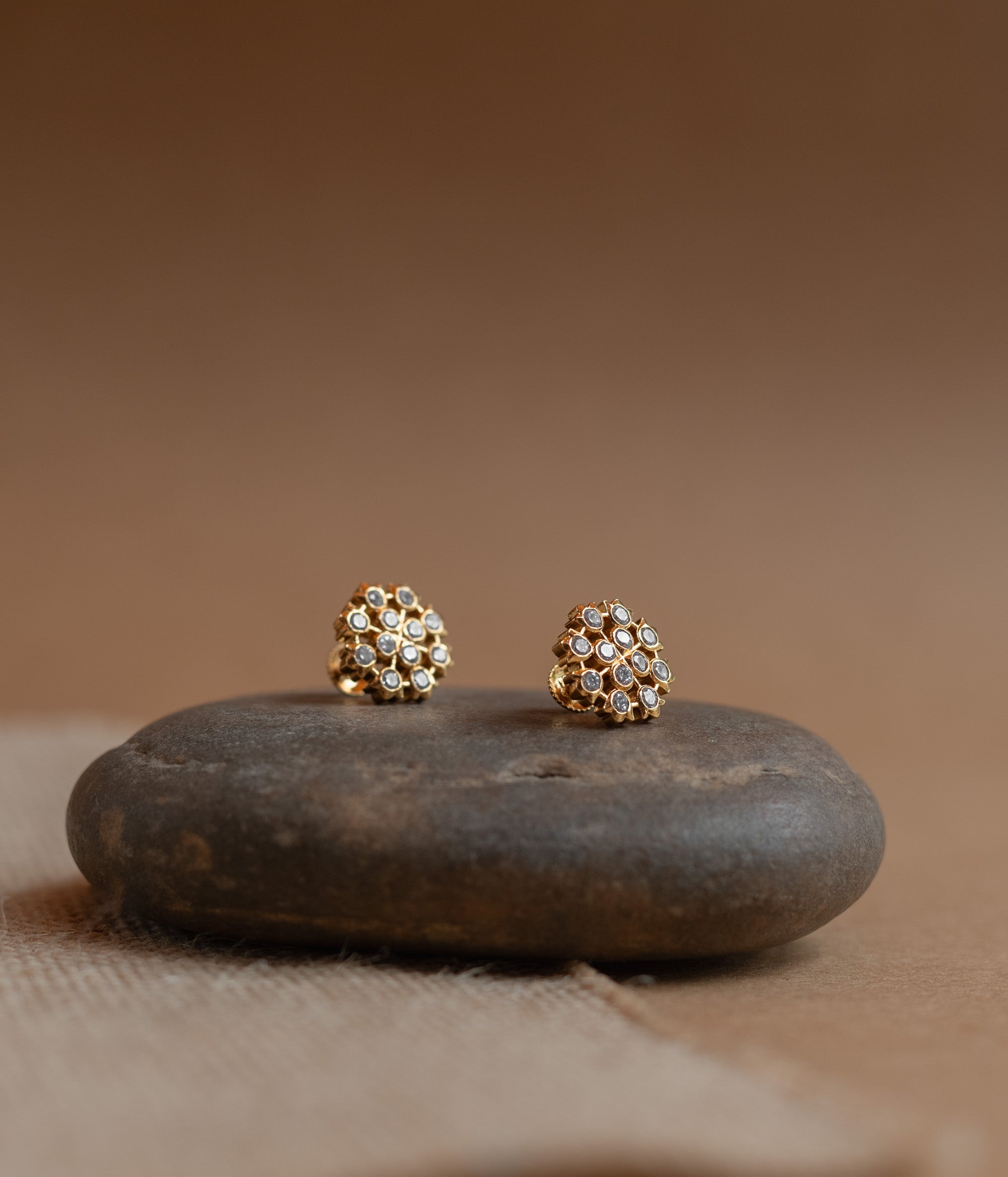 Gold floral stud earrings set with clear Swarovski stones, on a rock surface.