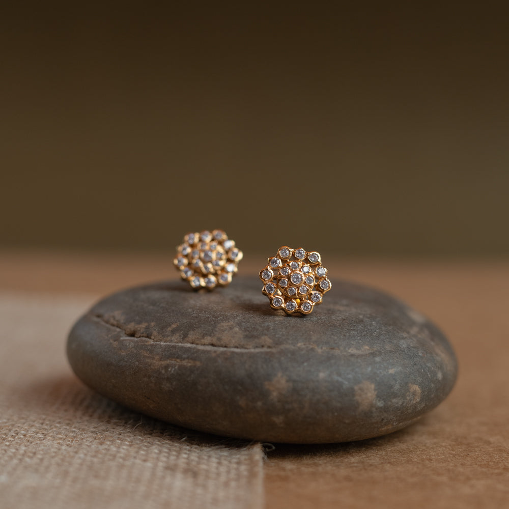 Gold floral stud earrings covered in clear Swarovski stones, displayed on a textured fabric.