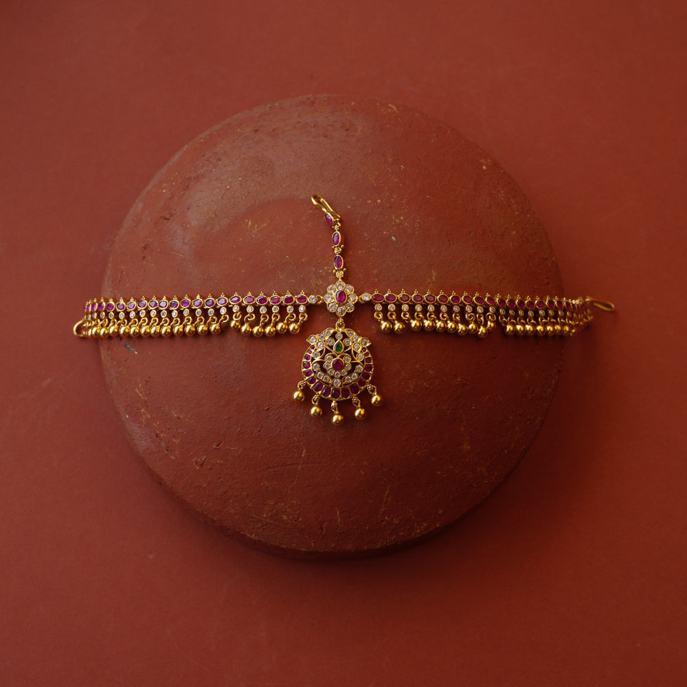 Traditional gold mathapatti with red, green, and Swarovski stones featuring temple bell-like danglers.
