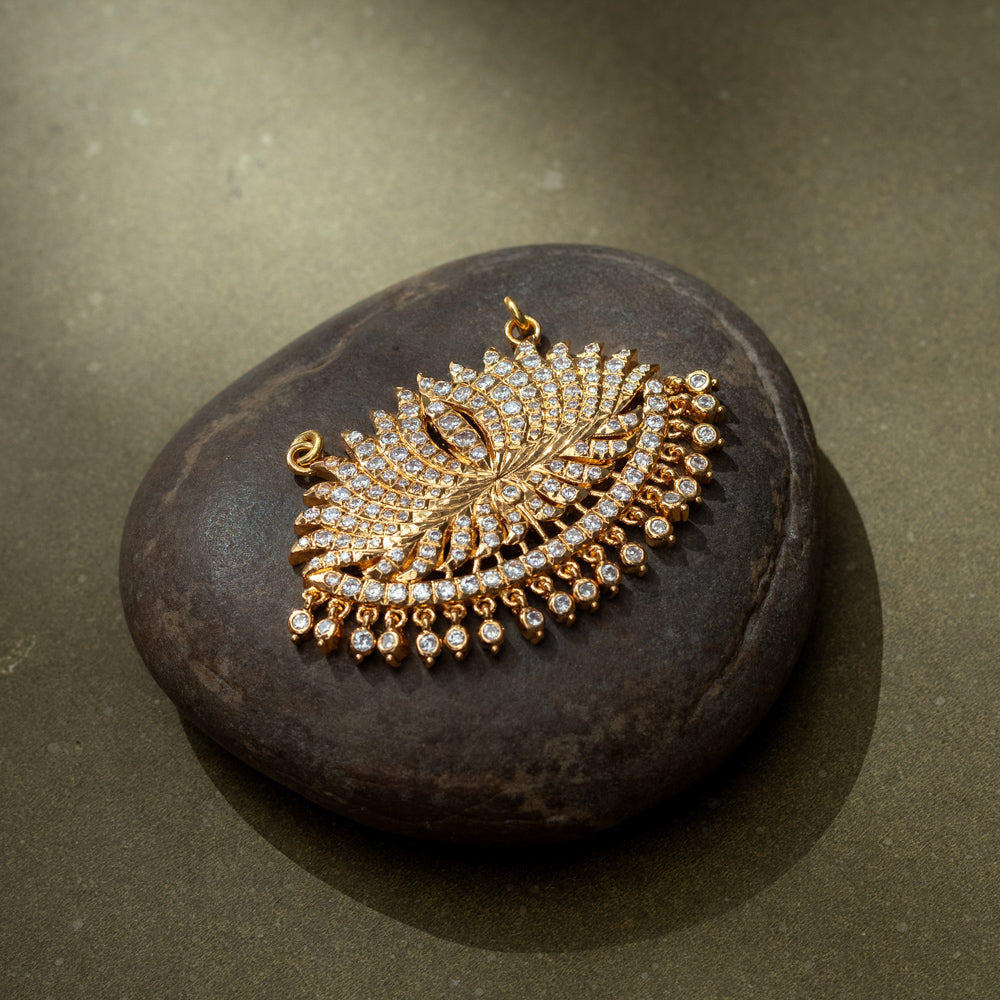 Gold fan-shaped pendant with CZ stones, inspired by peacock feather and sunburst motifs.
