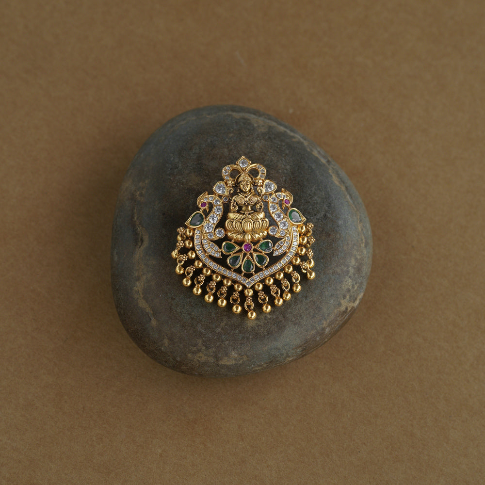 A gold pendant featuring a central deity figure on a lotus. It is decorated with clear, green, and red stones and has dangling gold beads.