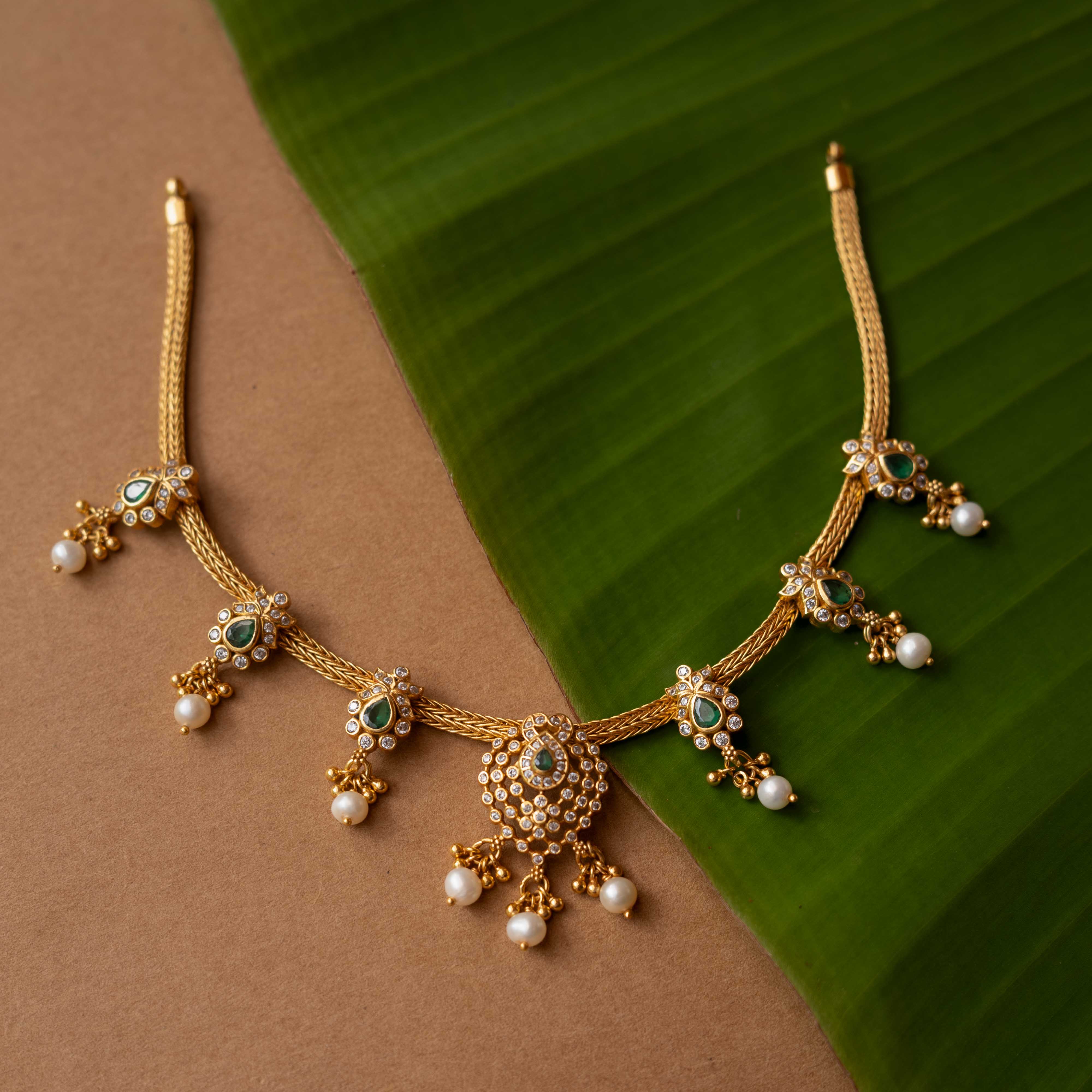 A necklace with a round pendant featuring a green stone, surrounded by clear stones, on a pearl chain.
