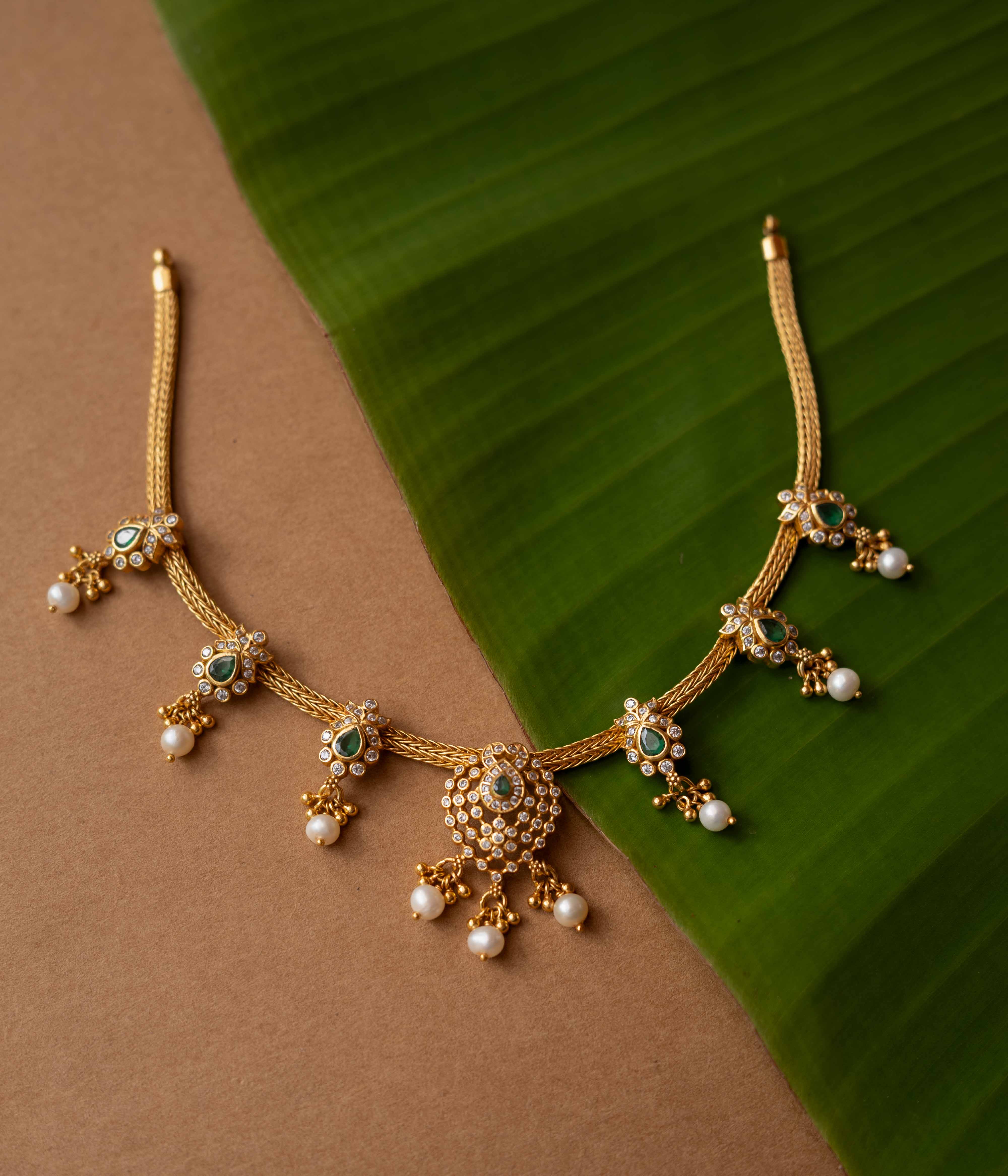 A necklace with a round pendant featuring a green stone, surrounded by clear stones, on a pearl chain.