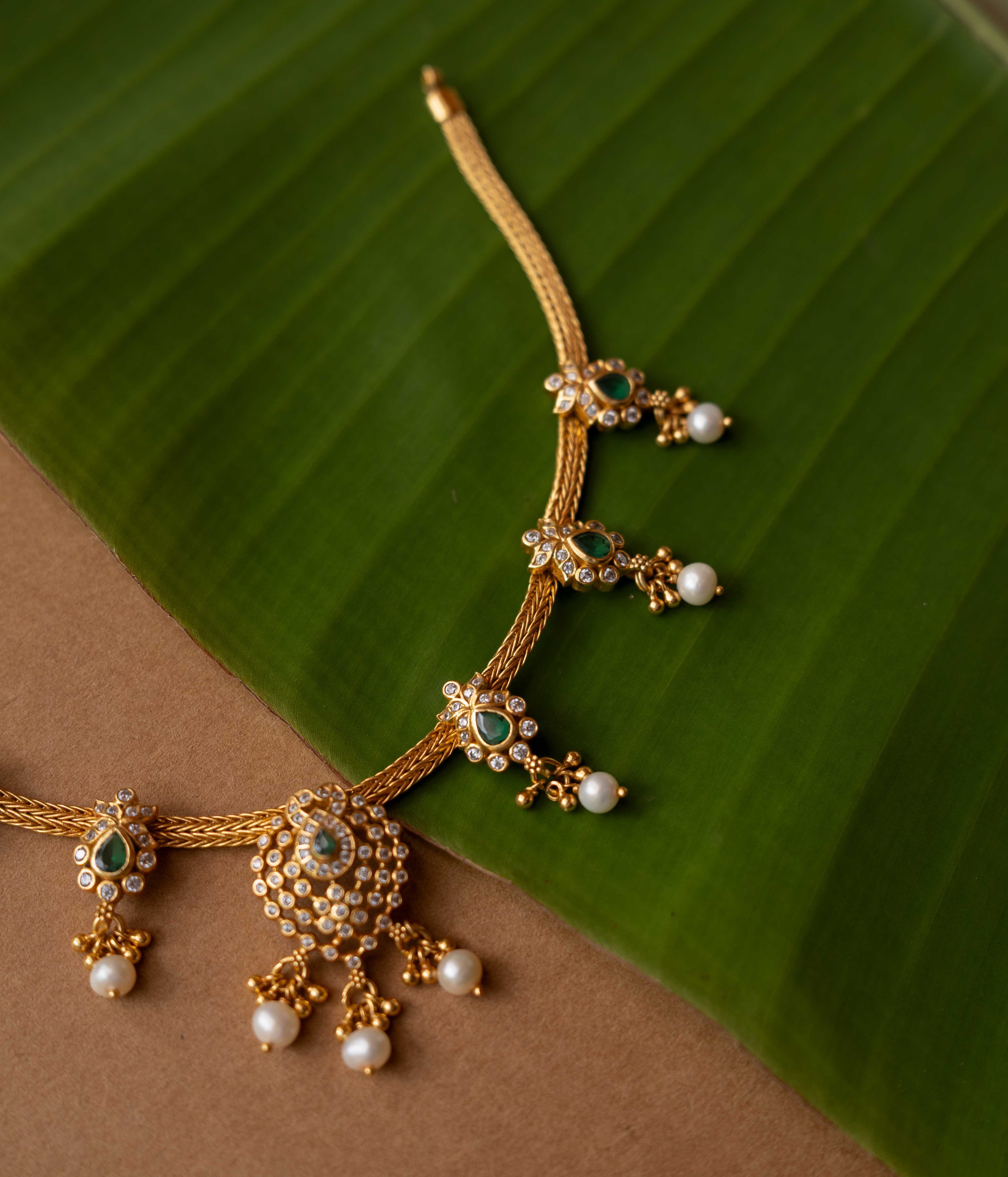 A necklace with a round pendant featuring a green stone, surrounded by clear stones, on a pearl chain.
