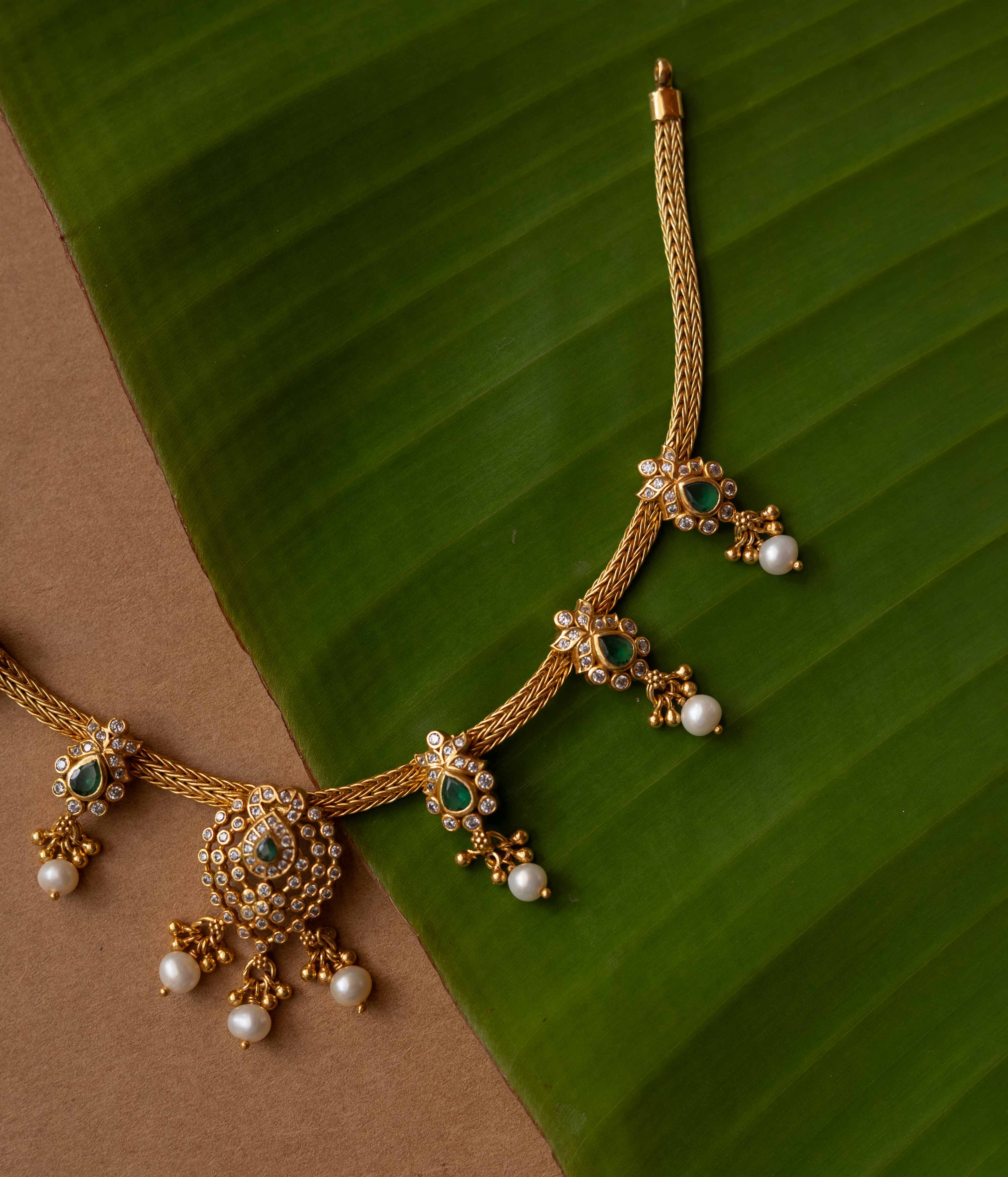 A necklace with a round pendant featuring a green stone, surrounded by clear stones, on a pearl chain.