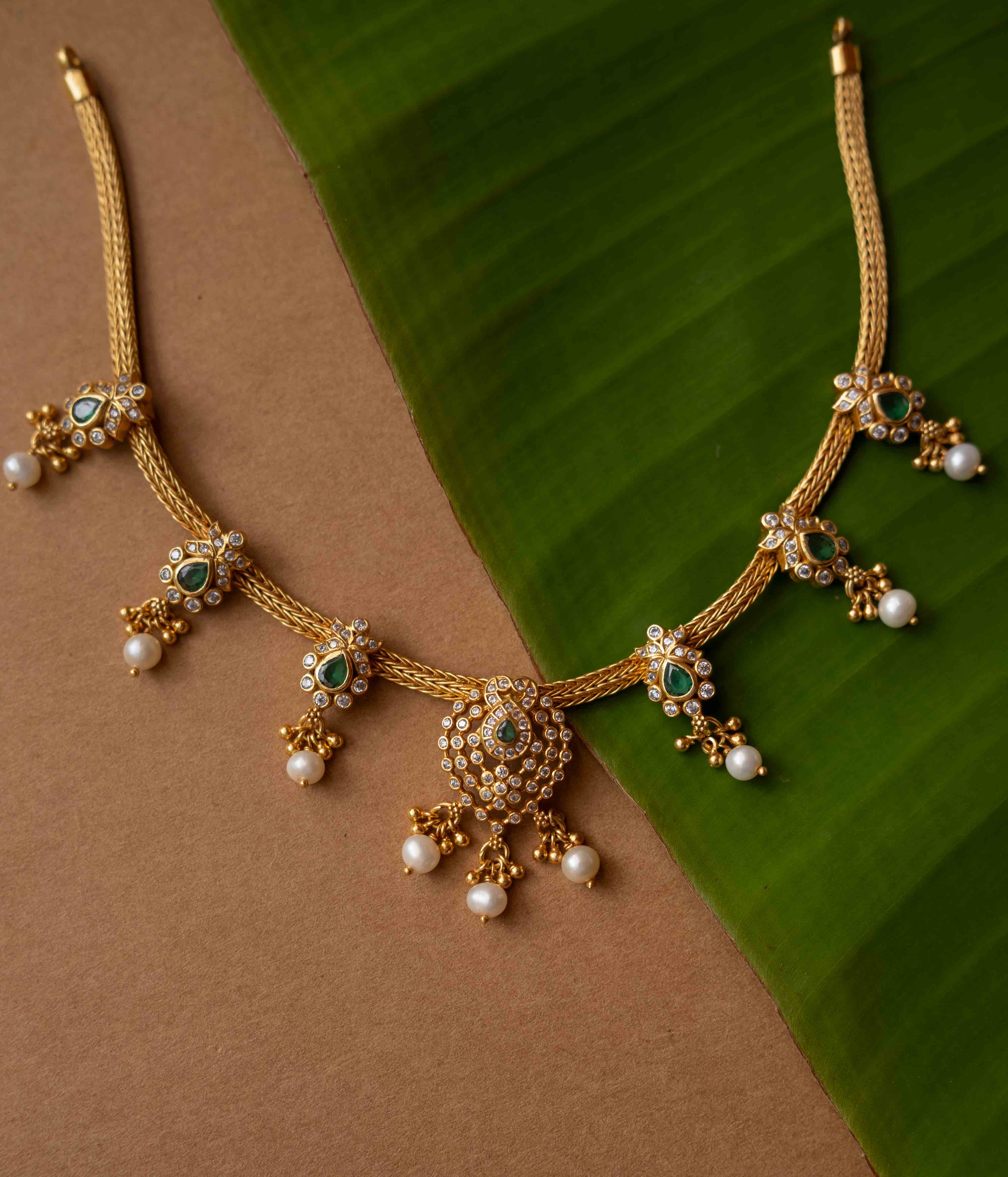 A necklace with a round pendant featuring a green stone, surrounded by clear stones, on a pearl chain.
