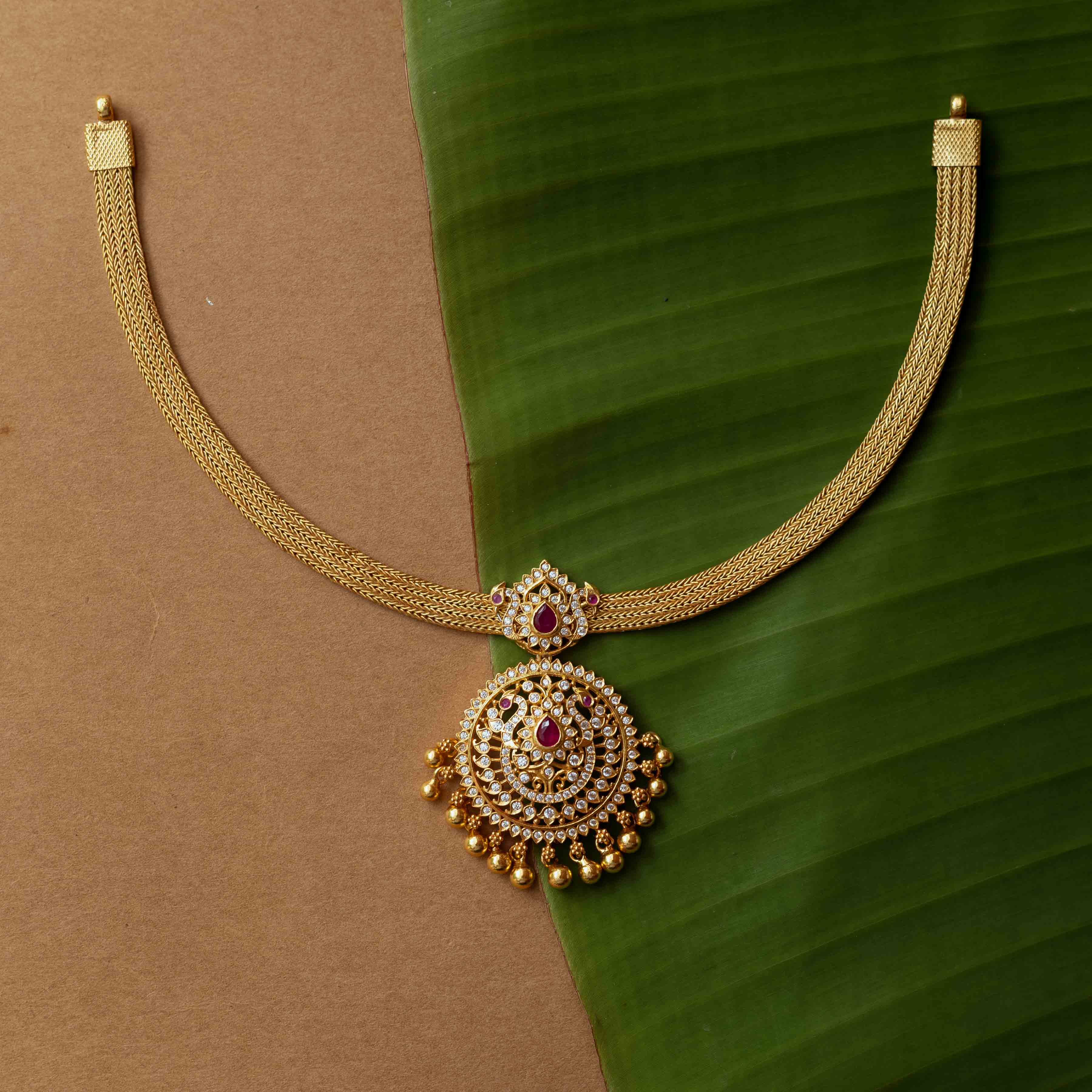 A necklace with a round pendant featuring a red stone, surrounded by clear stones, on a clear stone chain.
