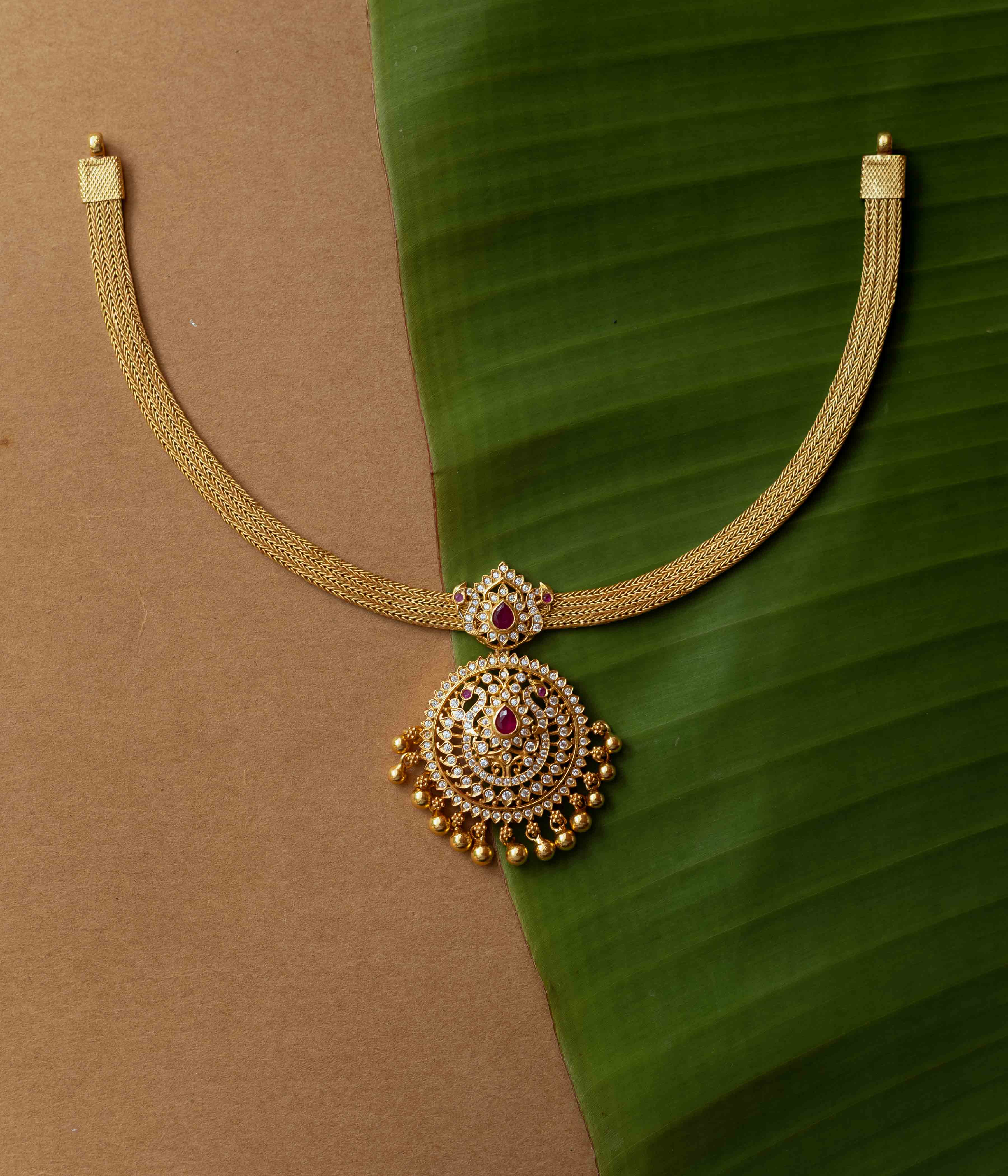 A necklace with a round pendant featuring a red stone, surrounded by clear stones, on a clear stone chain.