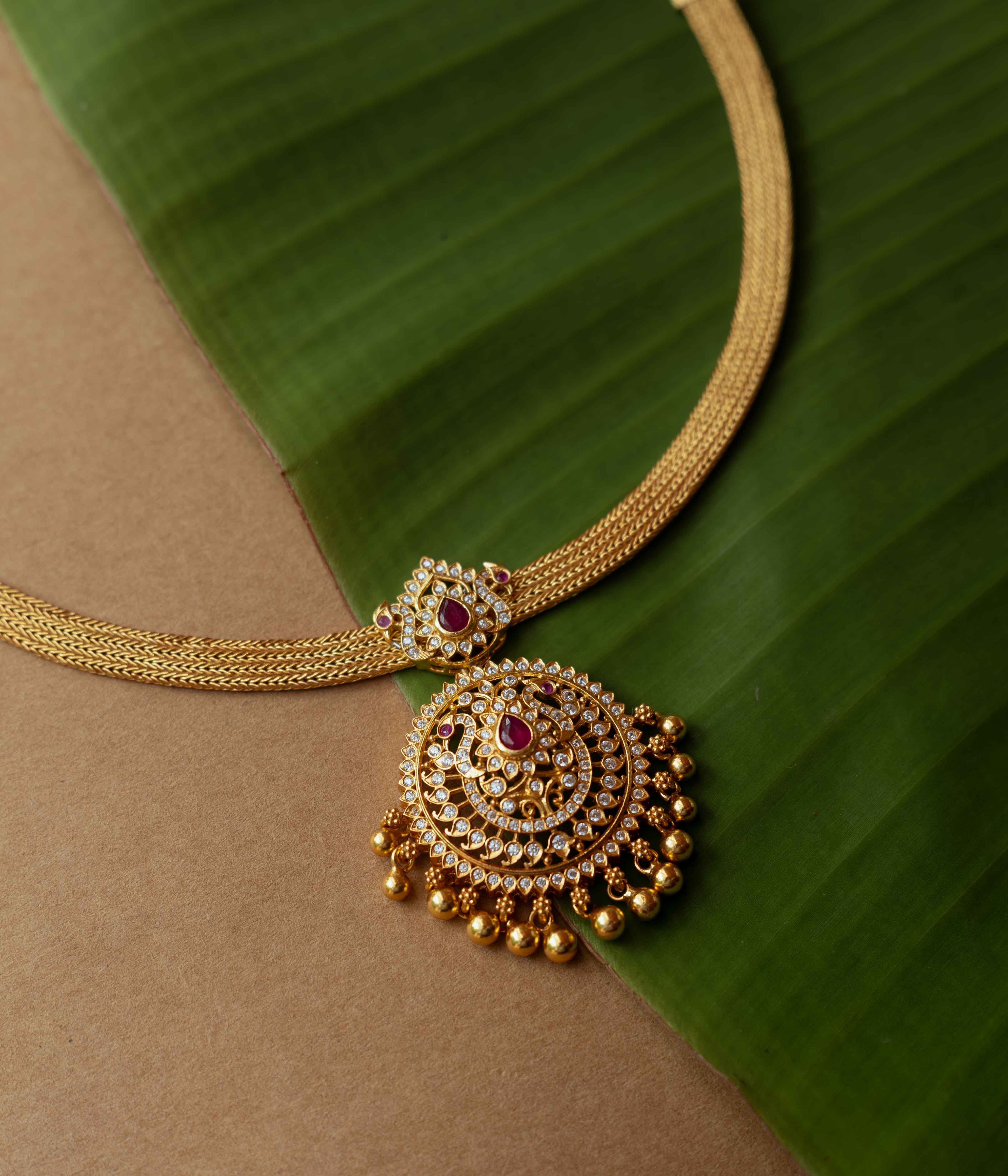 A necklace with a round pendant featuring a red stone, surrounded by clear stones, on a clear stone chain.