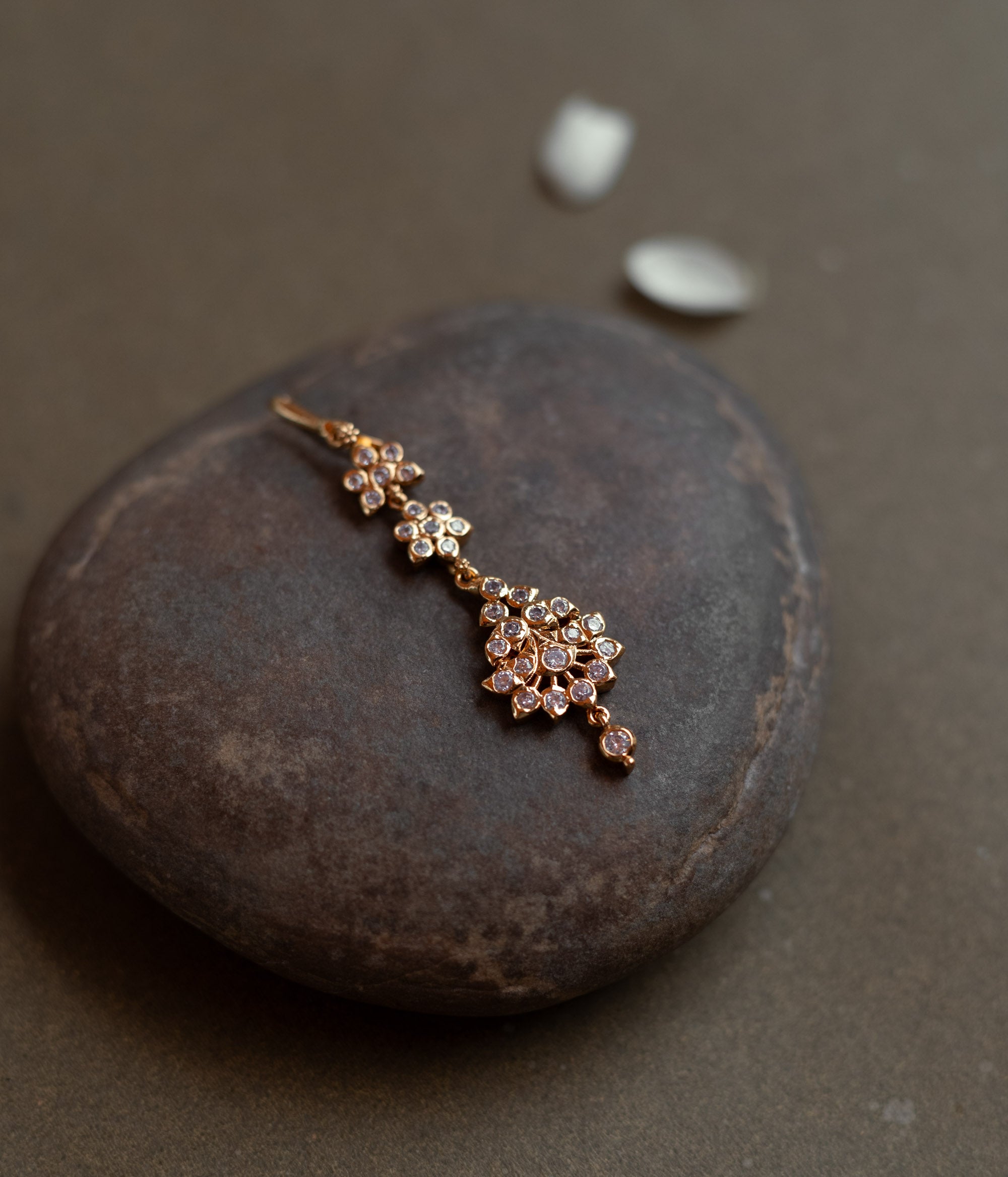 Elegant tikka with floral-shaped Swarovski stone design placed on a natural stone background.