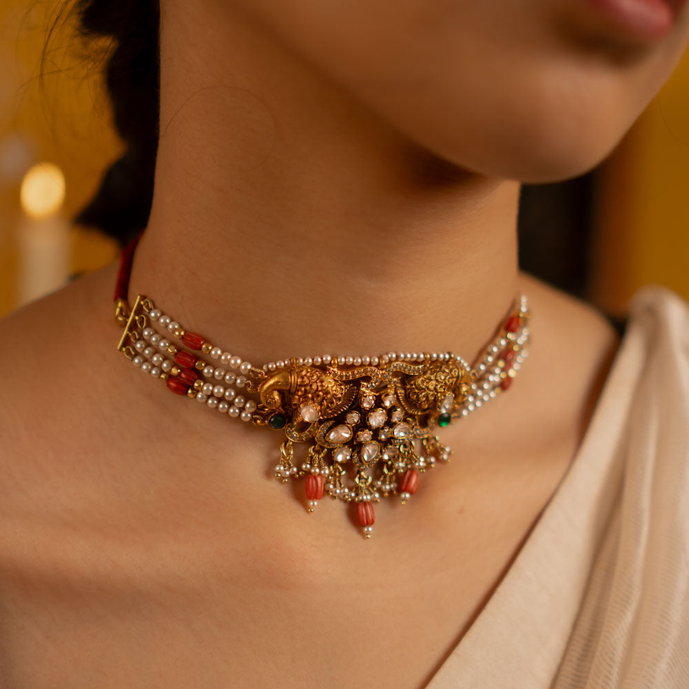 This exquisite gold-plated silver choker showcases a stunning arrangement of red and green kundan stones, red beads, CZ stones, and pearls. Embellished with rose-cut polkis and graceful peacock motifs, it seamlessly fuses traditional artistry with modern elegance.