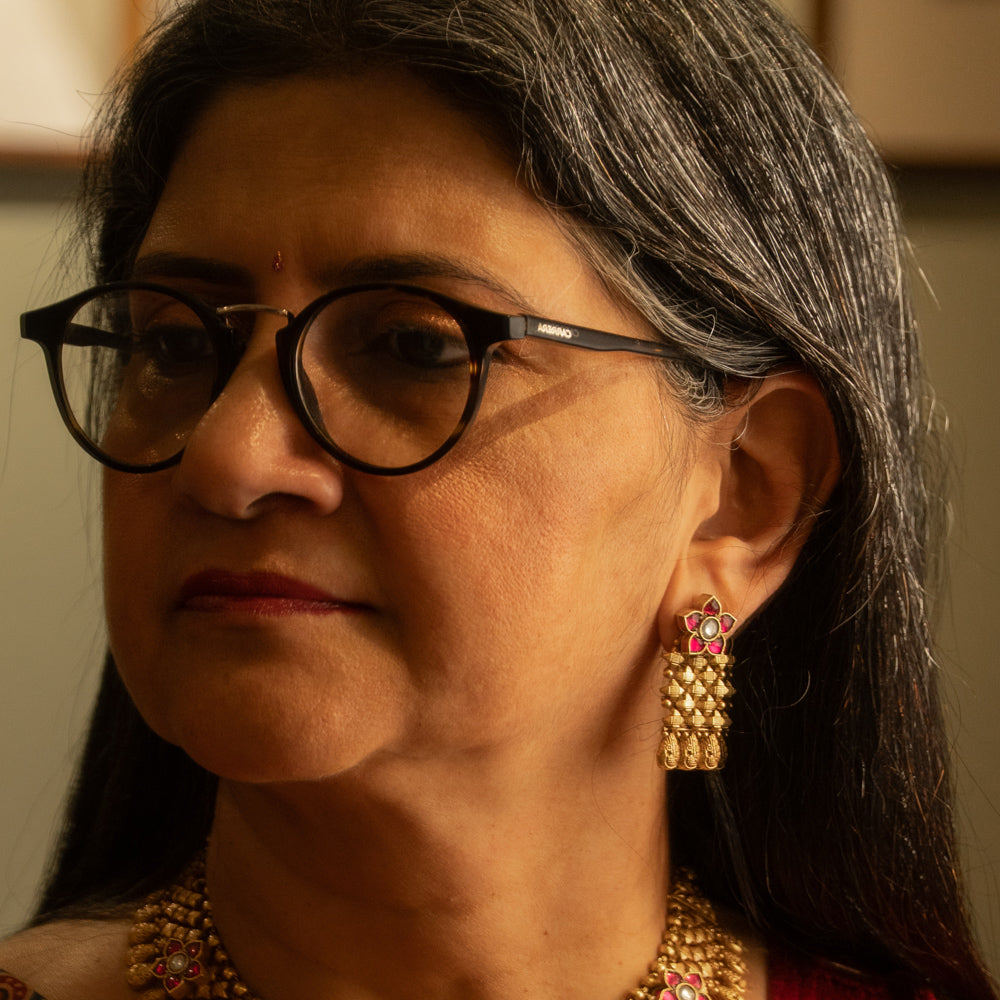 Woman wearing traditional gold tribal earrings with red and white Polki stones and floral motif.