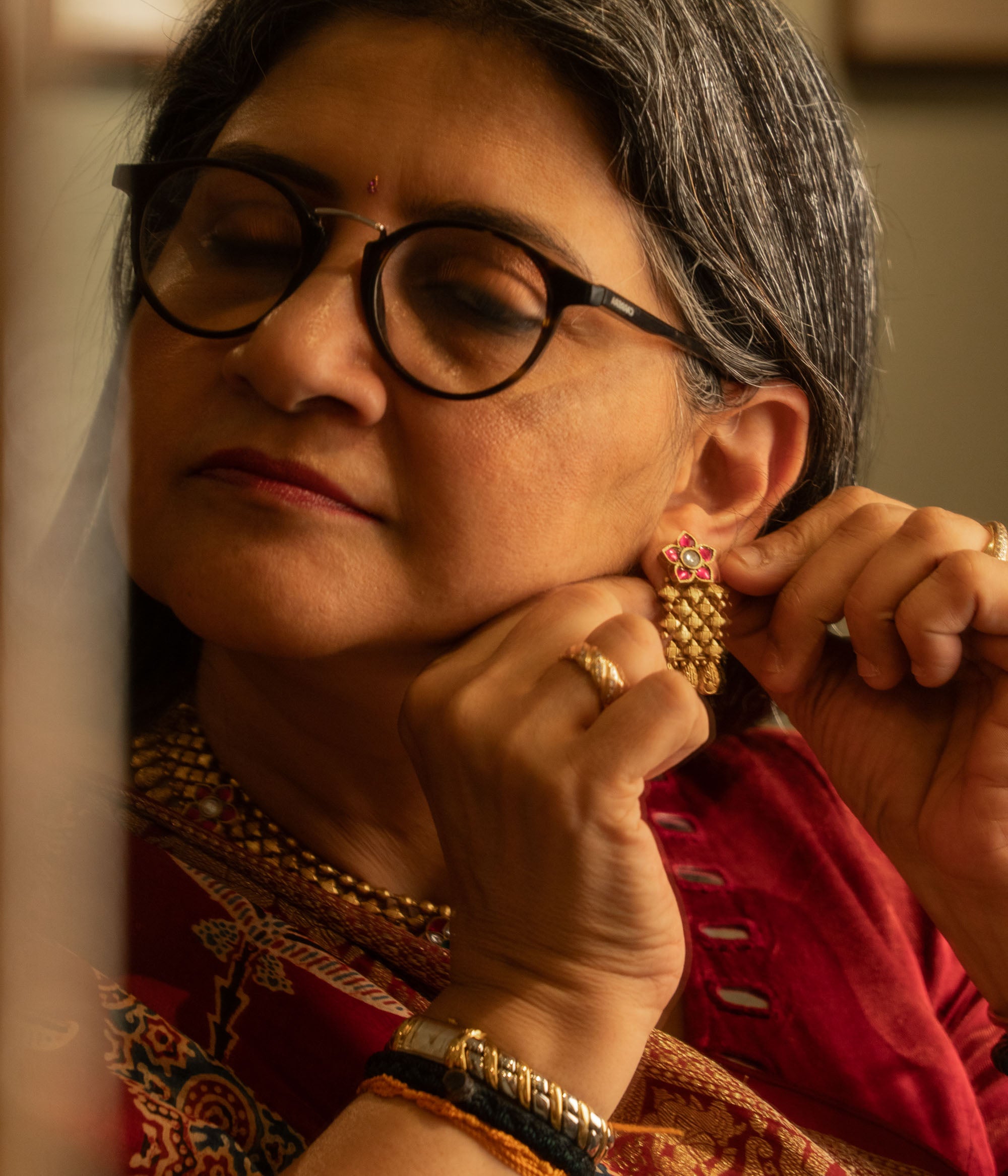 Woman wearing traditional gold tribal earrings with red and white Polki stones and floral motif.