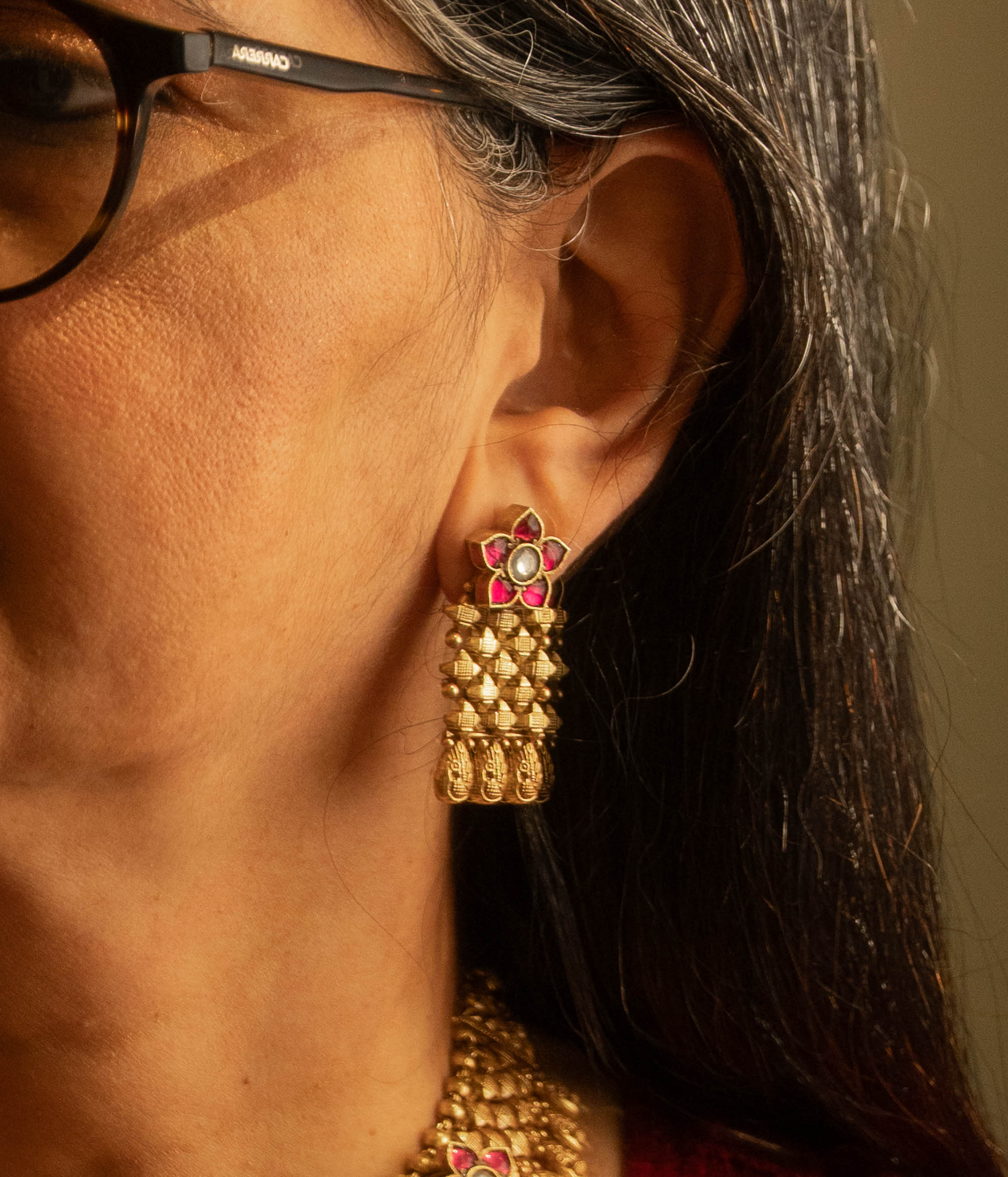Woman wearing traditional gold tribal earrings with red and white Polki stones and floral motif.