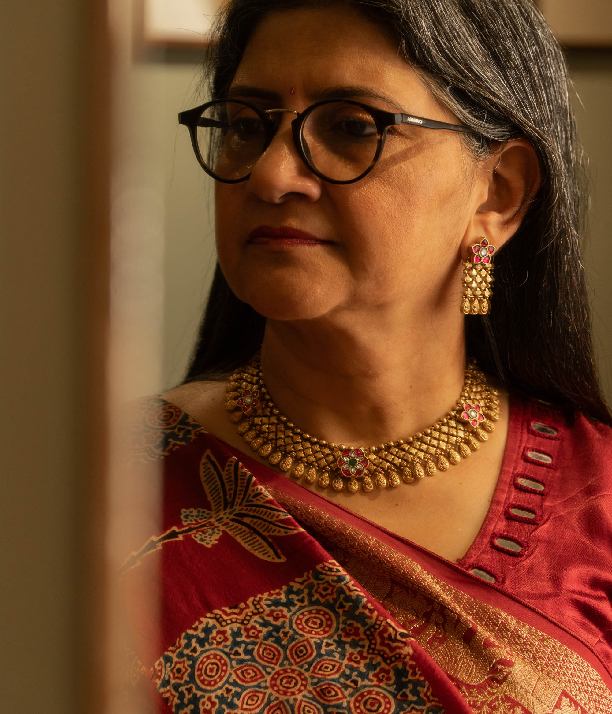 Woman wearing traditional gold tribal earrings with red and white Polki stones and floral motif.