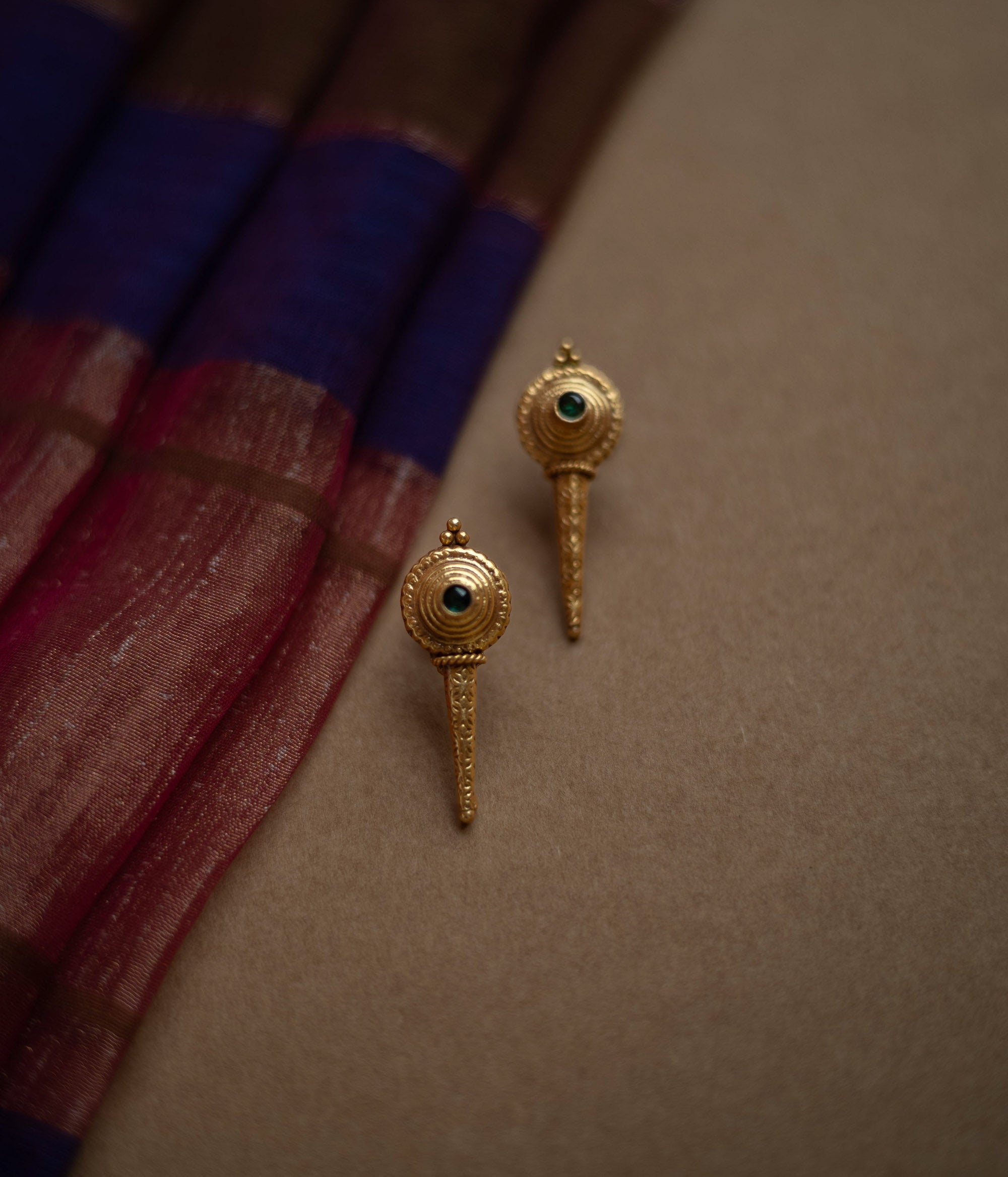 Antique gold stud earrings with a pointed, elongated design, each featuring a central green spinel stone.