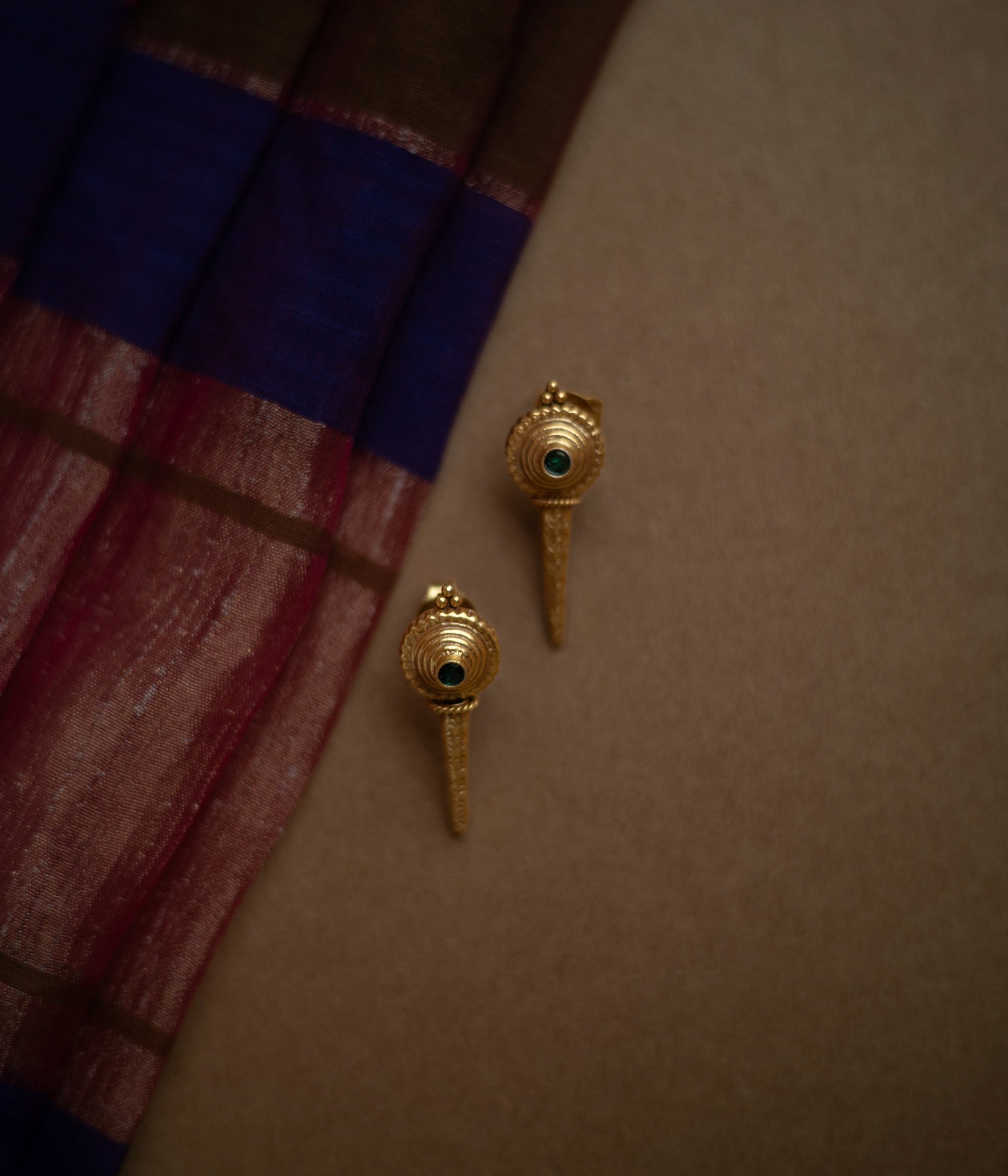 Antique gold stud earrings with a pointed, elongated design, each featuring a central green spinel stone.