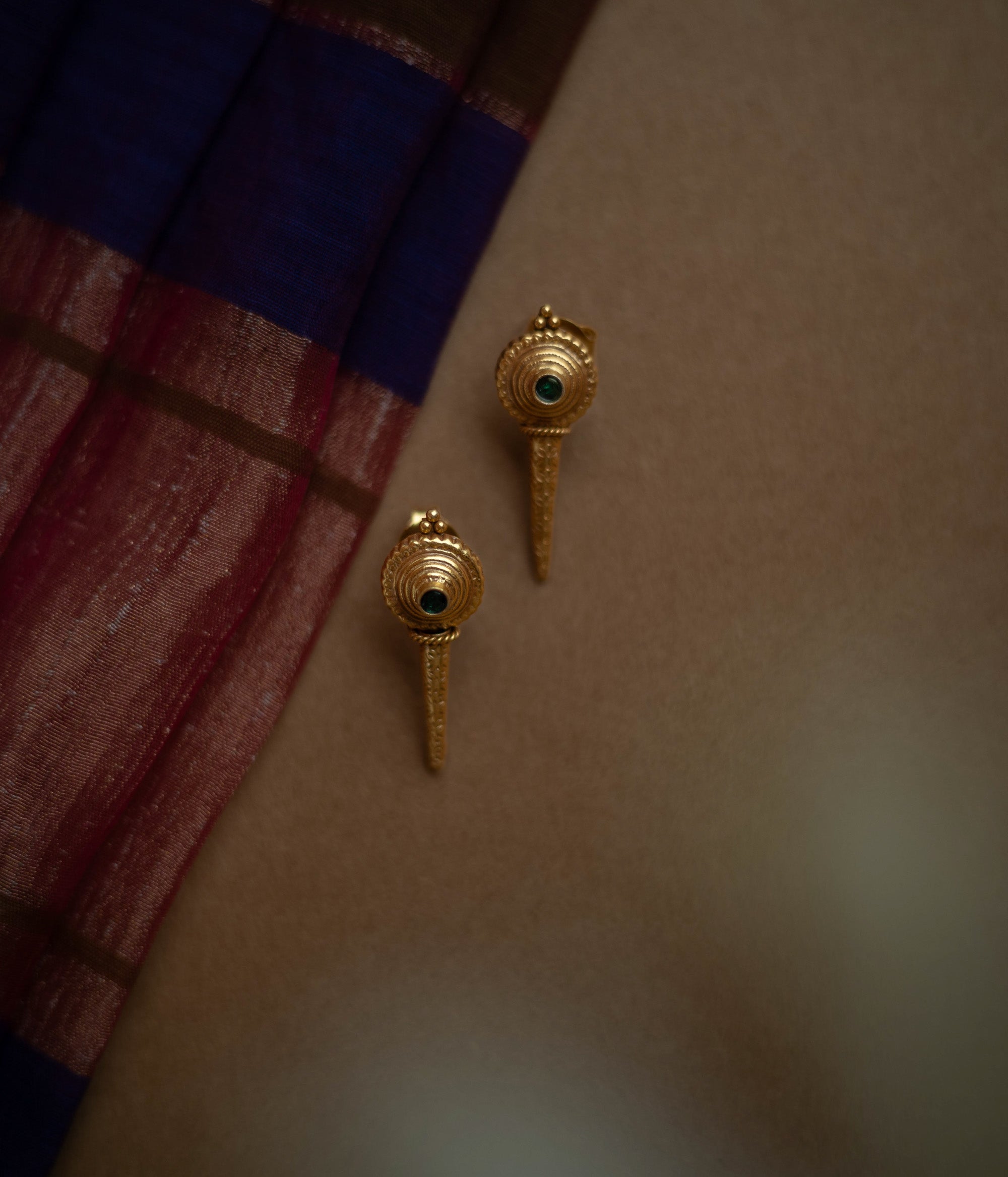 Antique gold stud earrings with a pointed, elongated design, each featuring a central green spinel stone.