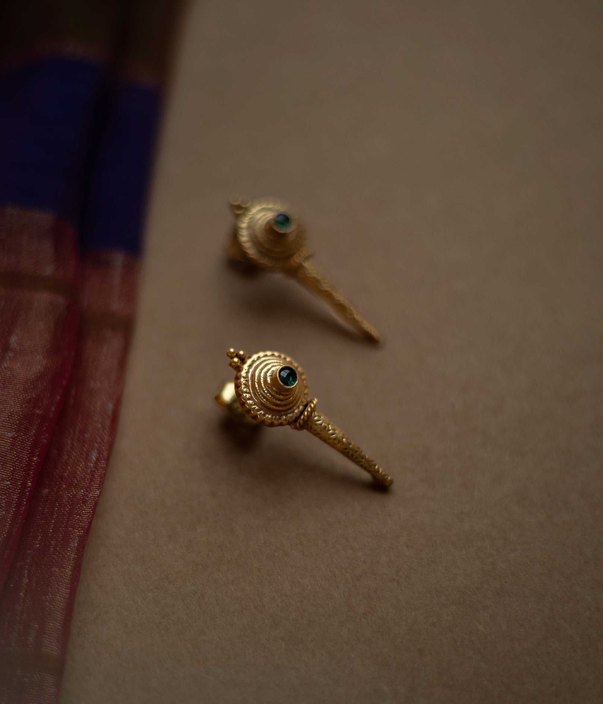 Antique gold stud earrings with a pointed, elongated design, each featuring a central green spinel stone.