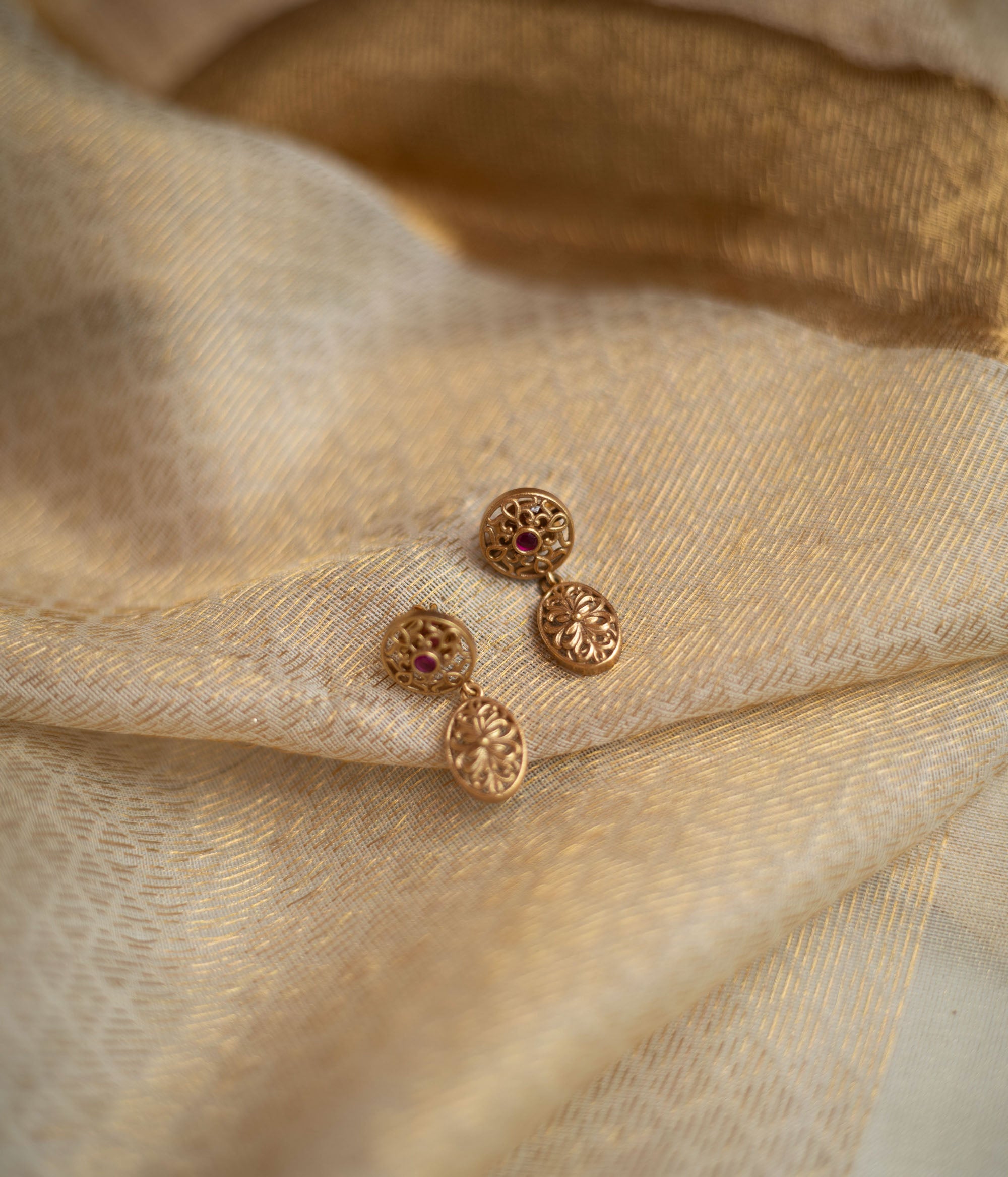 Gold drop earrings with red spinel stones and intricate circular designs.