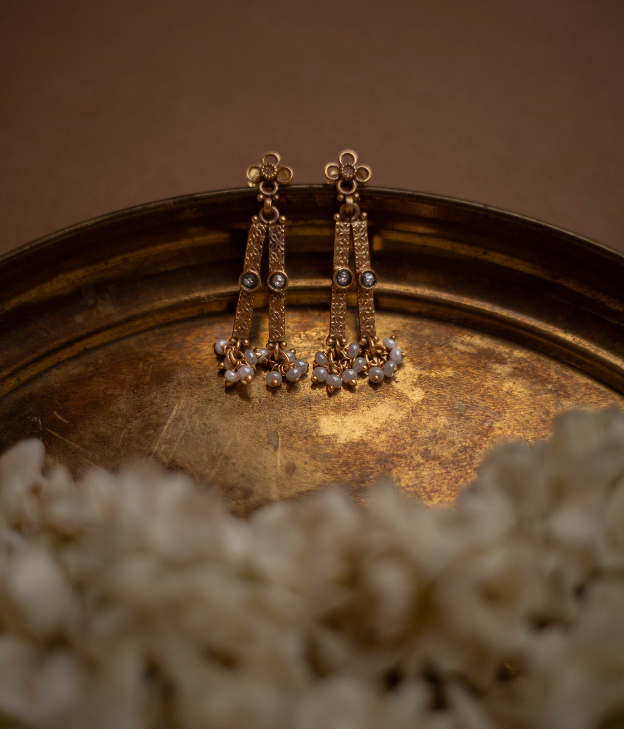 Antique gold drop earrings with white polki stones and pearl clusters, on a brass tray.