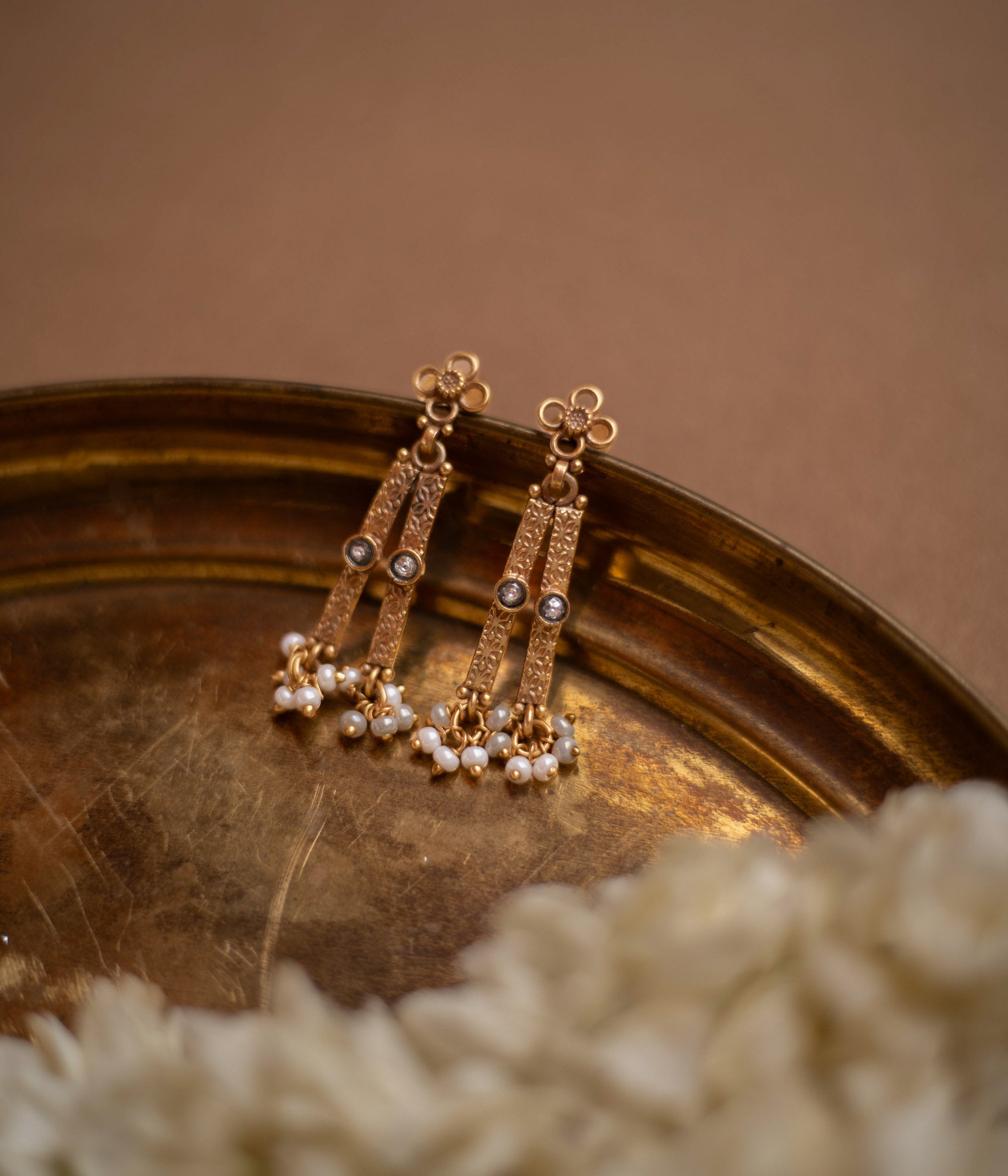 Antique gold drop earrings with white polki stones and pearl clusters, on a brass tray.
