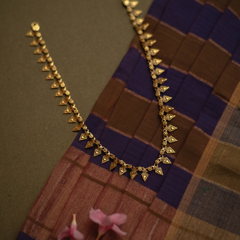 Gold tribal necklace with intricate leaf-like motifs, laid on a checkered fabric.