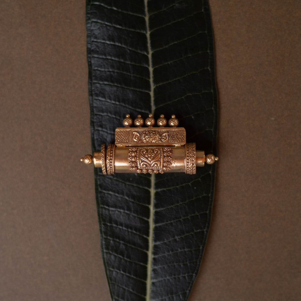 Antique gold mangalsutra pendant with an engraved scroll-like shape and hanging drops, on a dark green leaf.