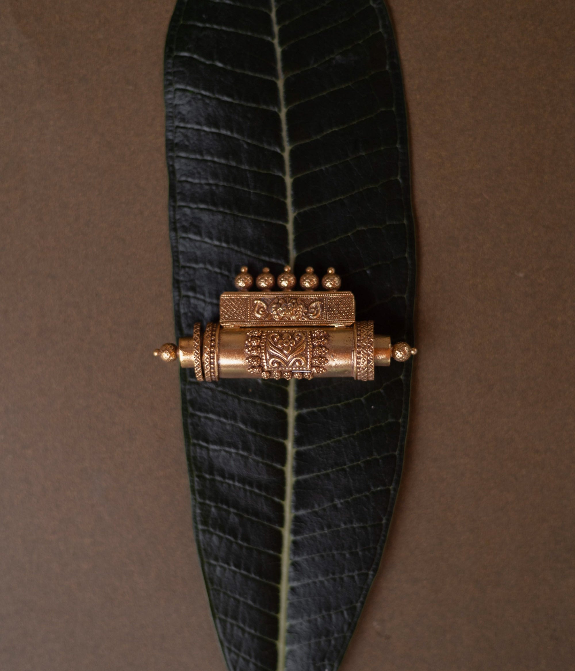 Antique gold mangalsutra pendant with an engraved scroll-like shape and hanging drops, on a dark green leaf.