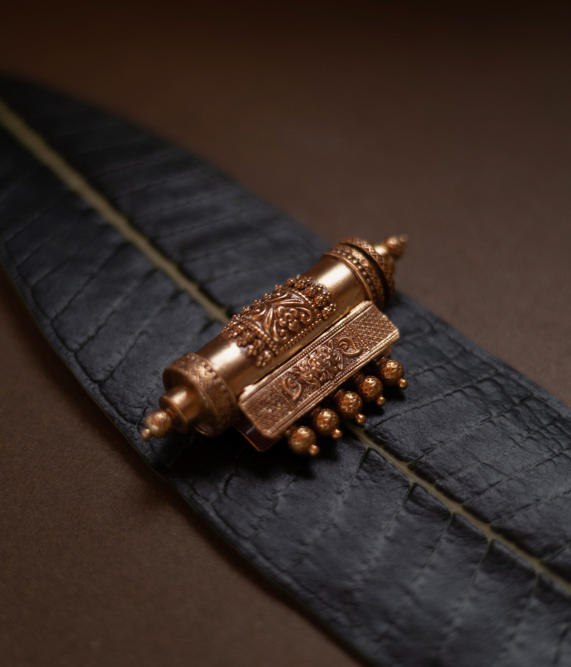 Antique gold mangalsutra pendant with an engraved scroll-like shape and hanging drops, on a dark green leaf.