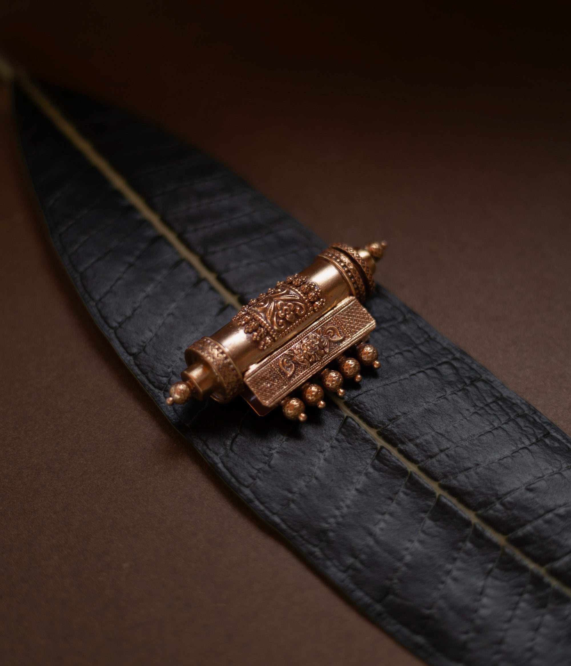 Antique gold mangalsutra pendant with an engraved scroll-like shape and hanging drops, on a dark green leaf.