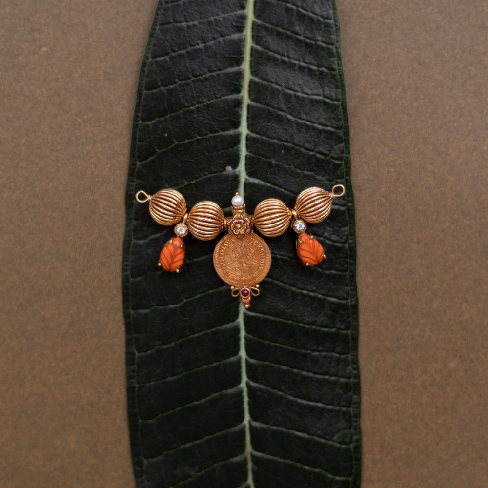 Traditional Mangalsutra pendant with Lakshmi coin, pearls, and red spinel stones on a leaf.