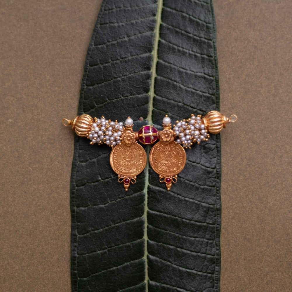 Twin coin Mangalsutra pendant with pearls, red spinel stones, and gold detailing on leaf backdrop.