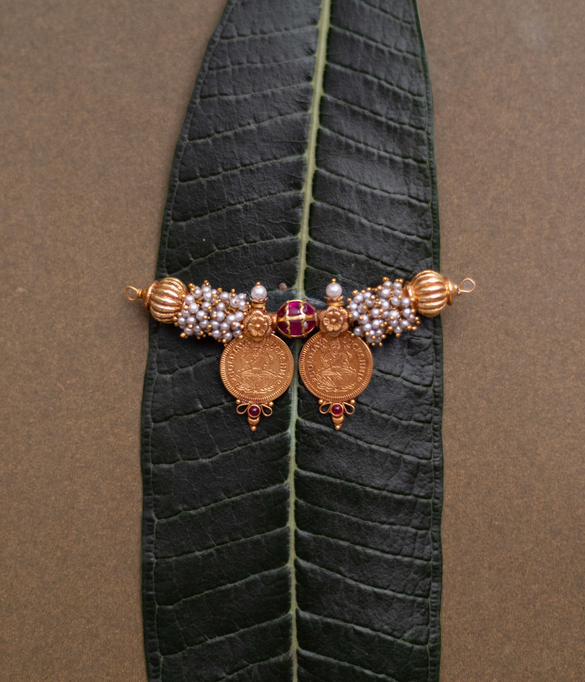 Twin coin Mangalsutra pendant with pearls, red spinel stones, and gold detailing on leaf backdrop.