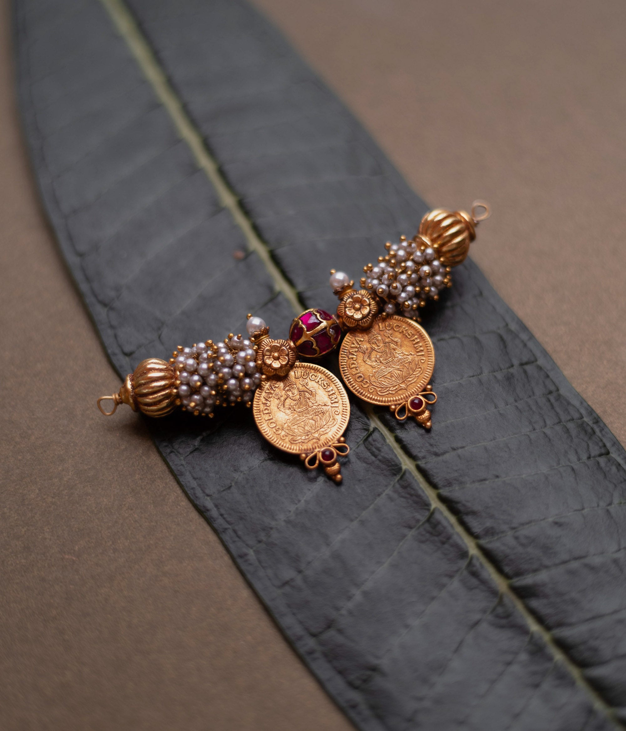 Twin coin Mangalsutra pendant with pearls, red spinel stones, and gold detailing on leaf backdrop.