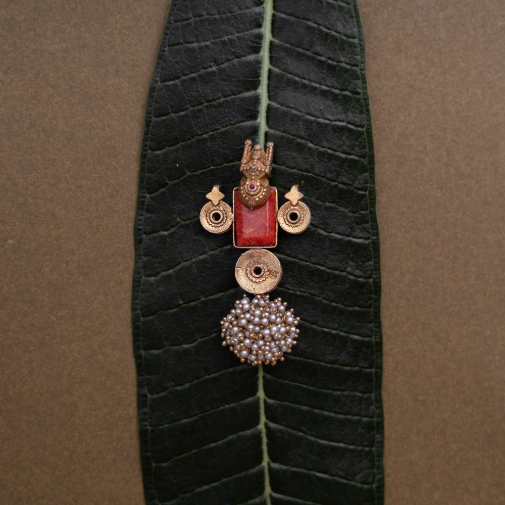 Temple-style pendant with red stone, deity motif, antique gold finish, and pearl cluster base.