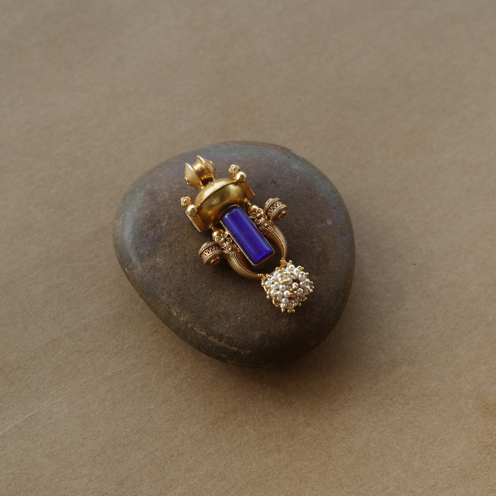 Gold tribal pendant with vertical blue stone, pearl cluster, and ornate sacred motifs.