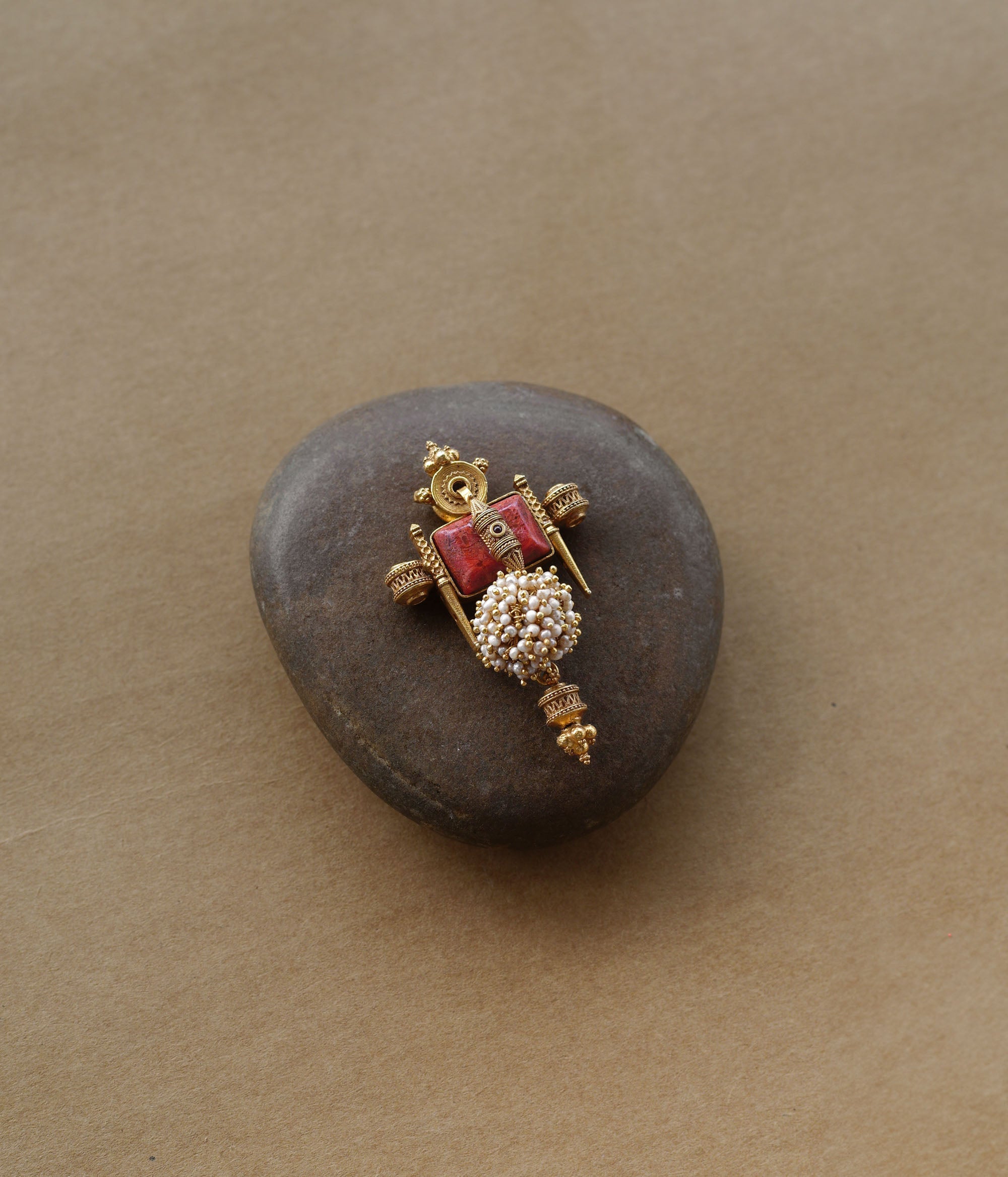 Tribal-inspired gold pendant with red spinal stone, pearl cluster, and sacred symmetrical design.
