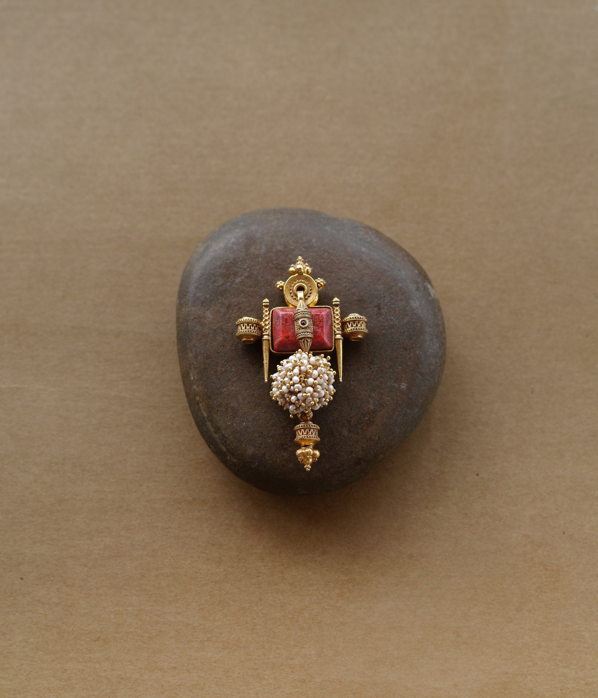 Tribal-inspired gold pendant with red spinal stone, pearl cluster, and sacred symmetrical design.
