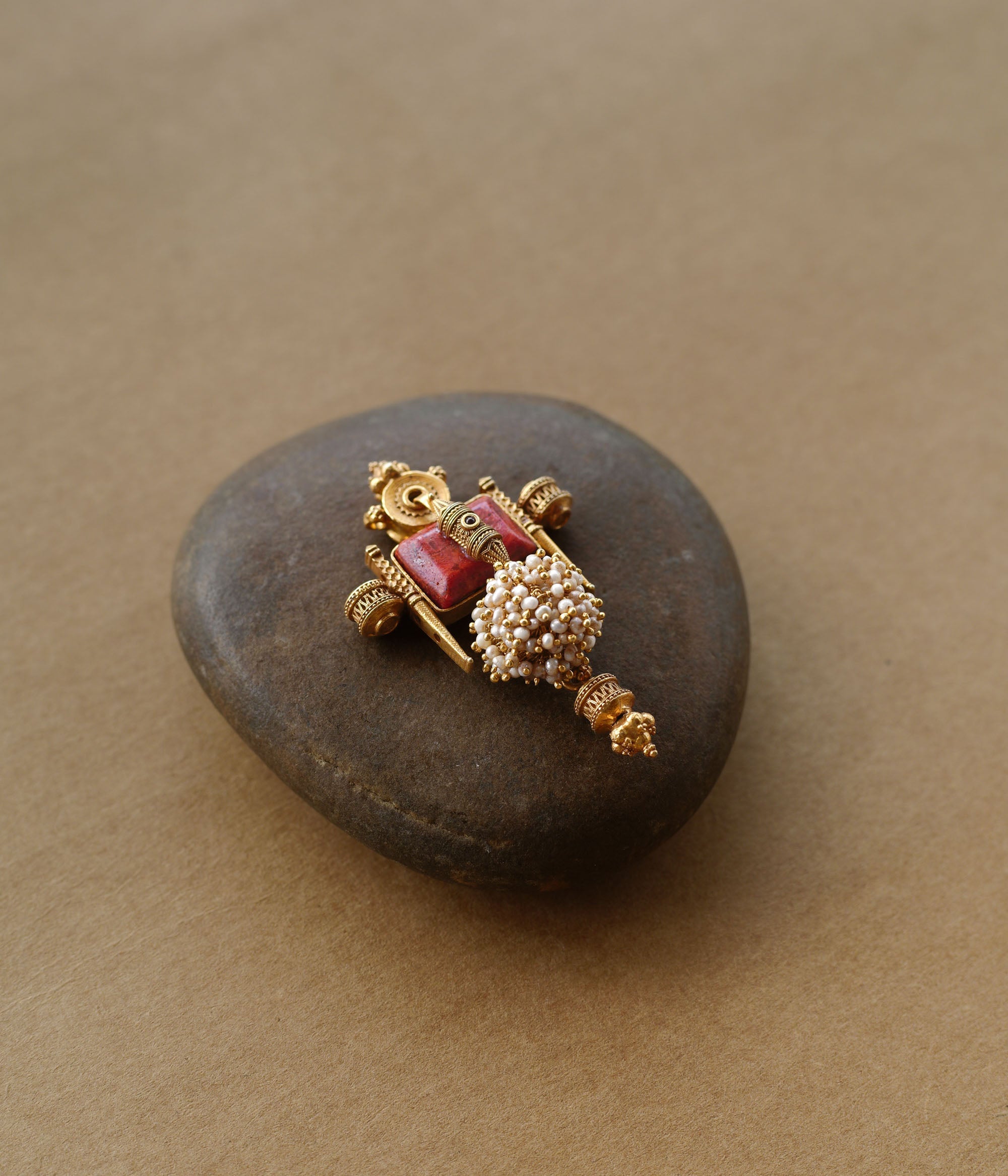 Tribal-inspired gold pendant with red spinal stone, pearl cluster, and sacred symmetrical design.
