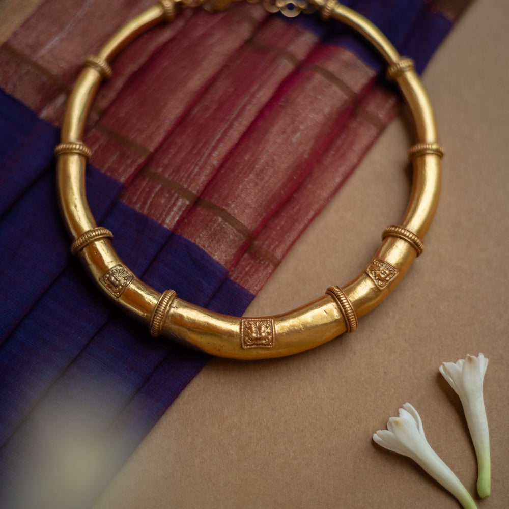 Thick, antique gold hasli necklace with textured bands and square motifs, displayed on fabric.