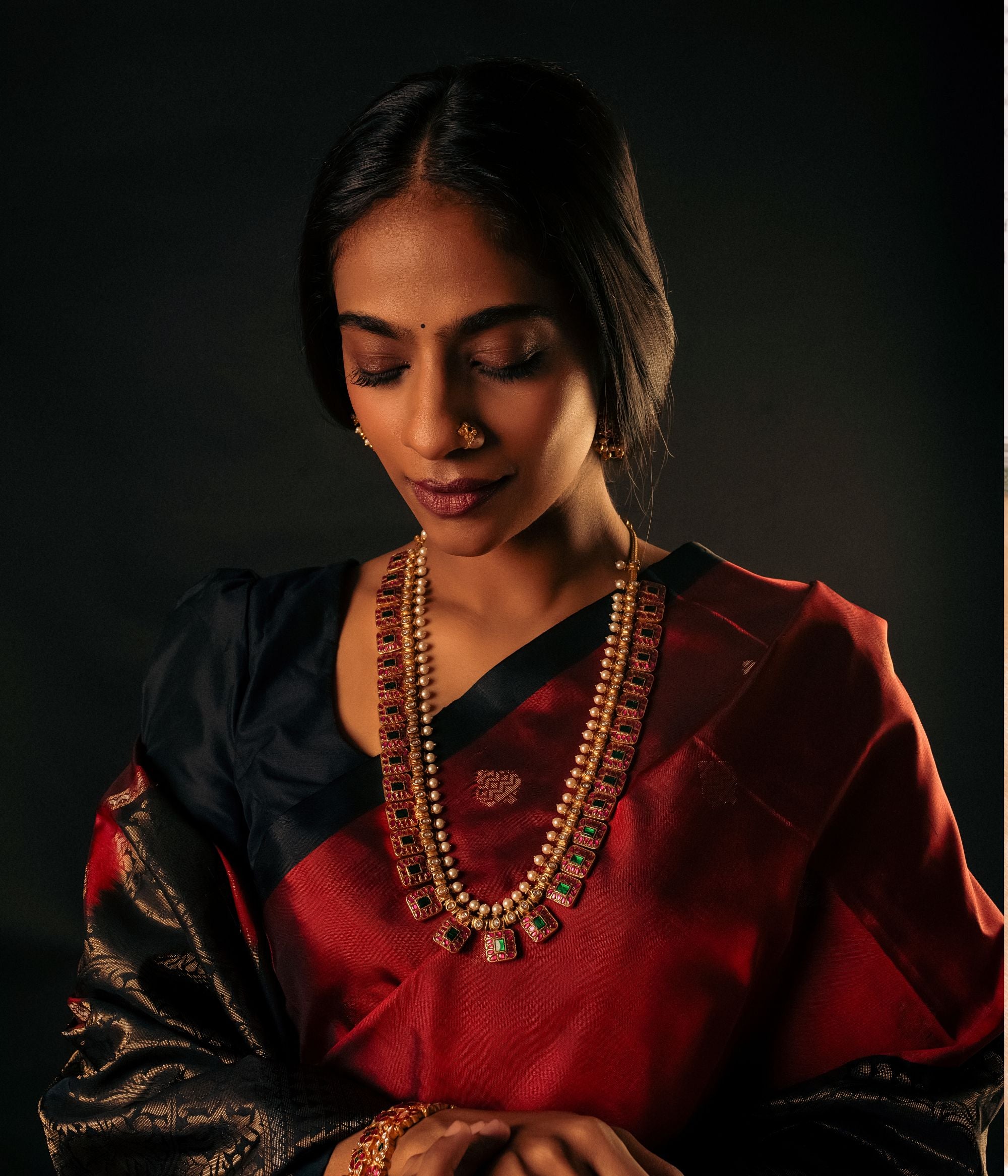 Exquisite gold-plated silver necklace featuring a unique chain composed of square-shaped drops, each adorned with vibrant red and green Kundan stones. The elegant design is further enhanced by a row of white Kundan stones and delicate pearls gracefully holding the chain, adding a regal and timeless charm to the piece.