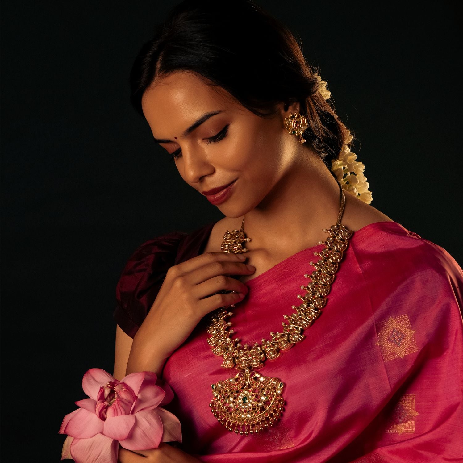 Detailed view of an antique silver, gold-plated necklace featuring a central floral-designed pendant adorned with red Kundan stones, white Kundan stones, and green Kundan stones. The necklace showcases intricate peacock motifs and mango-shaped designs embedded with stones, adding to its regal charm. Smaller pendants dangle along the lower edge, while white pearls and golden beads enhance its elegance, making it a perfect blend of tradition and sophistication.