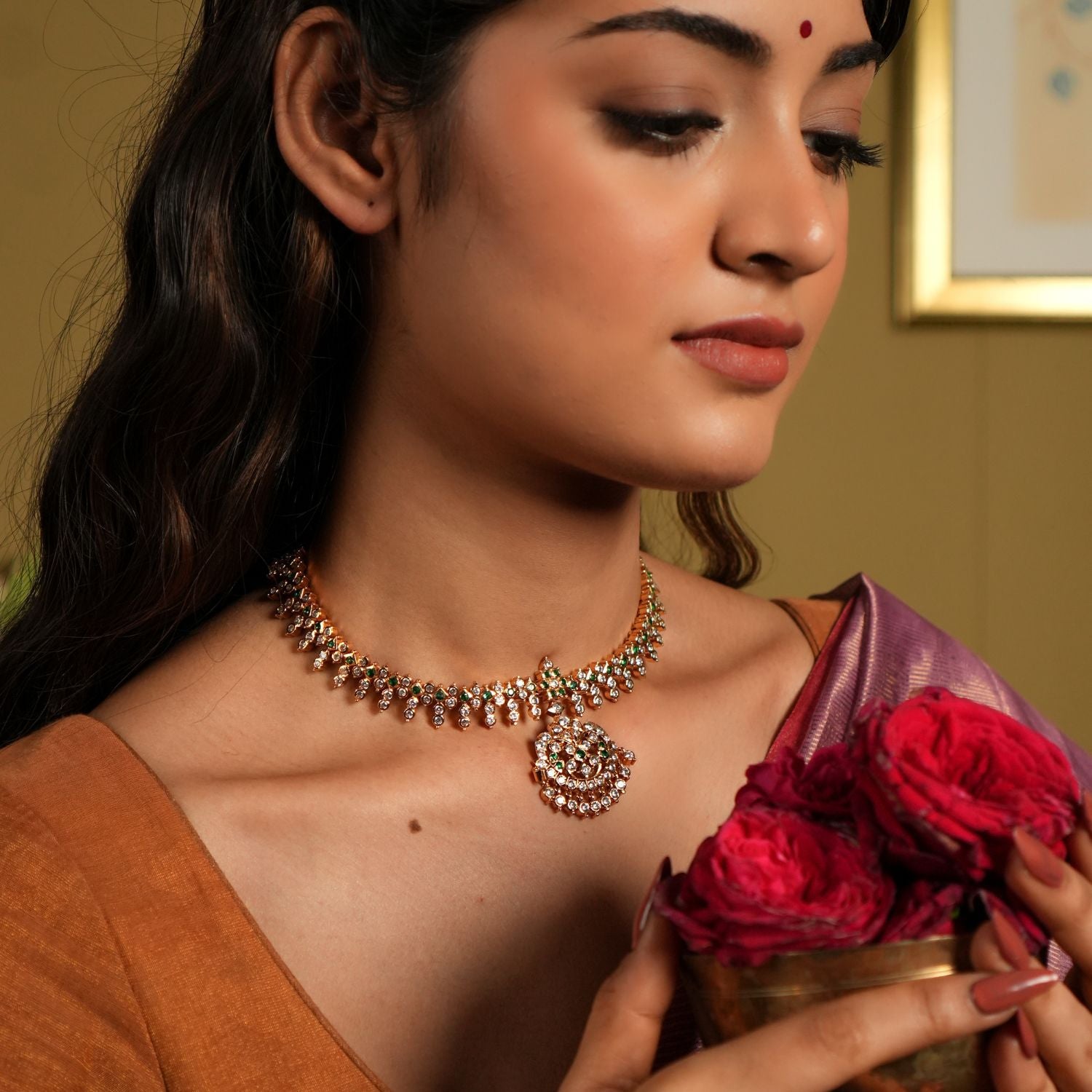 This exquisite Swarovski choker, crafted from 92.5 sterling silver with a rich 22-carat gold plating, is adorned with traditional floral motifs that whisper vintage Chettinad elegance. The intricate detailing and shimmering Swarovski stones bring a timeless charm, perfectly blending heritage craftsmanship with modern sophistication. Ideal for weddings and festive occasions, this choker gracefully accentuates your neckline, adding a touch of regal allure to any ensemble.