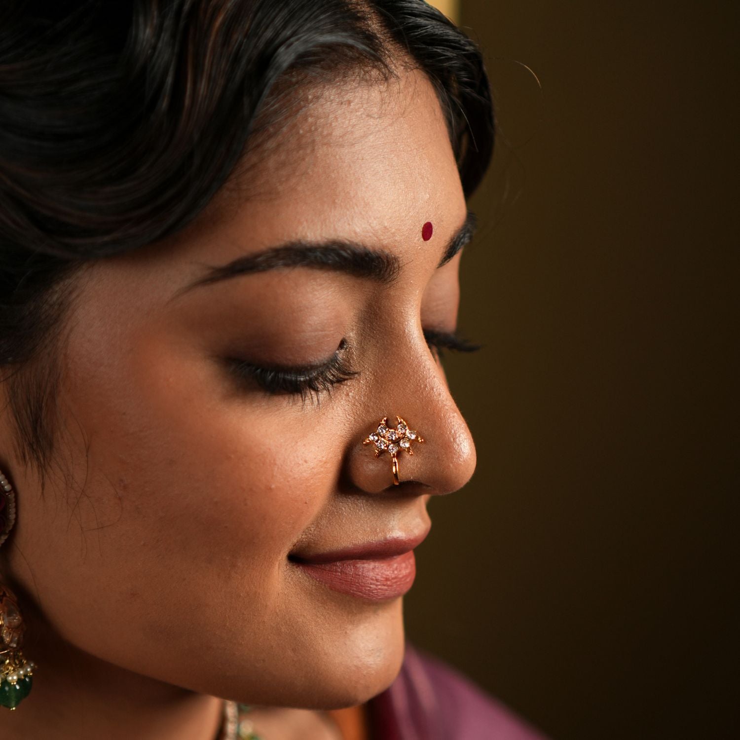 features a stunning 92.5 sterling silver nose pin with an elegant gold-plated finish. The nose pin is designed in a unique, intricate pattern adorned with sparkling stones, offering a delicate yet eye-catching appeal. Its refined craftsmanship and graceful design make it a versatile accessory, perfect for traditional attire or festive occasions.