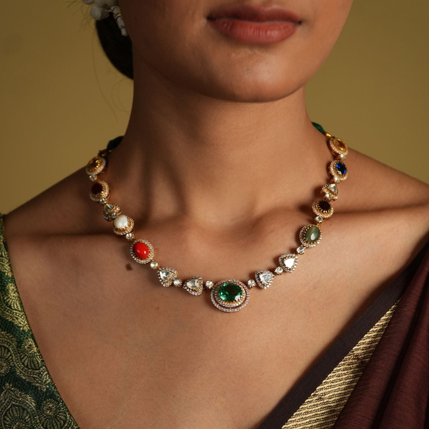 This elegant 92.5 sterling silver necklace is beautifully gold-plated and features a classic Navratna design. Adorned with nine vibrant gemstones, including emerald, ruby, sapphire, coral, and more, each stone represents celestial significance and brings a pop of color to your ensemble.