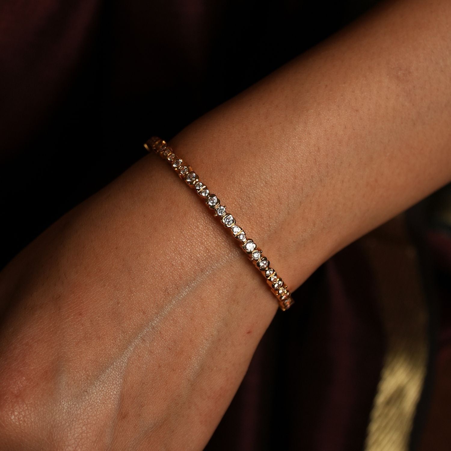 This is a close-up image of a wrist adorned with a delicate gold bracelet encrusted with swarovski Clean lines, delicate sparkle,
and heritage-inspired setting evoke the refined beauty of Tamil Nadu's iconic jewellery.
